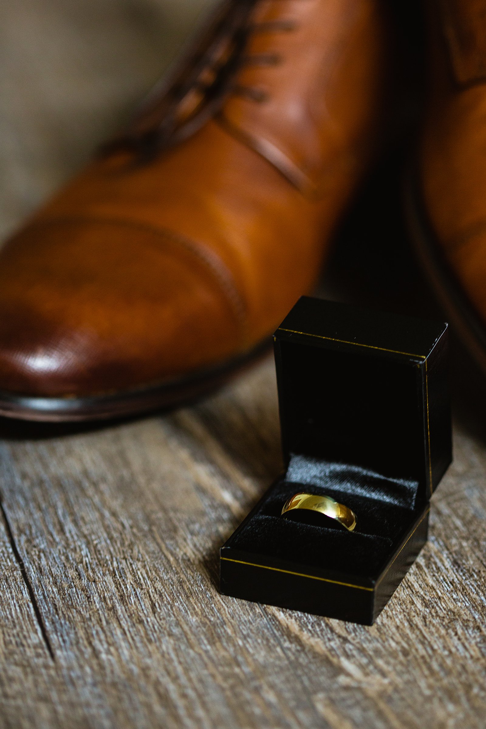 Simple gold wedding band in front of tan leather shoes by PMA Photography.
