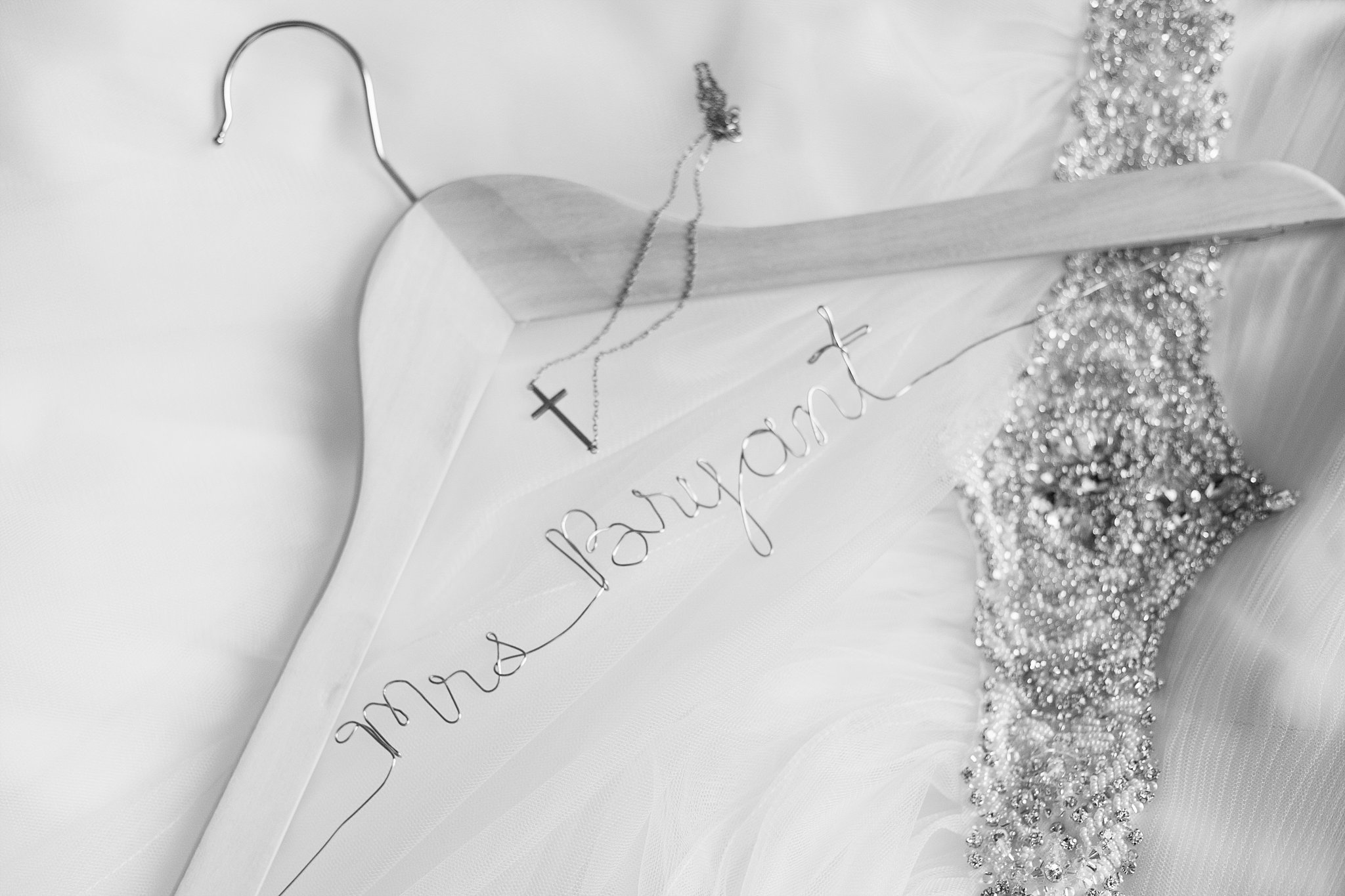 Black and white image of bride's custom dress hanger with her cross necklace by PMA Photography.