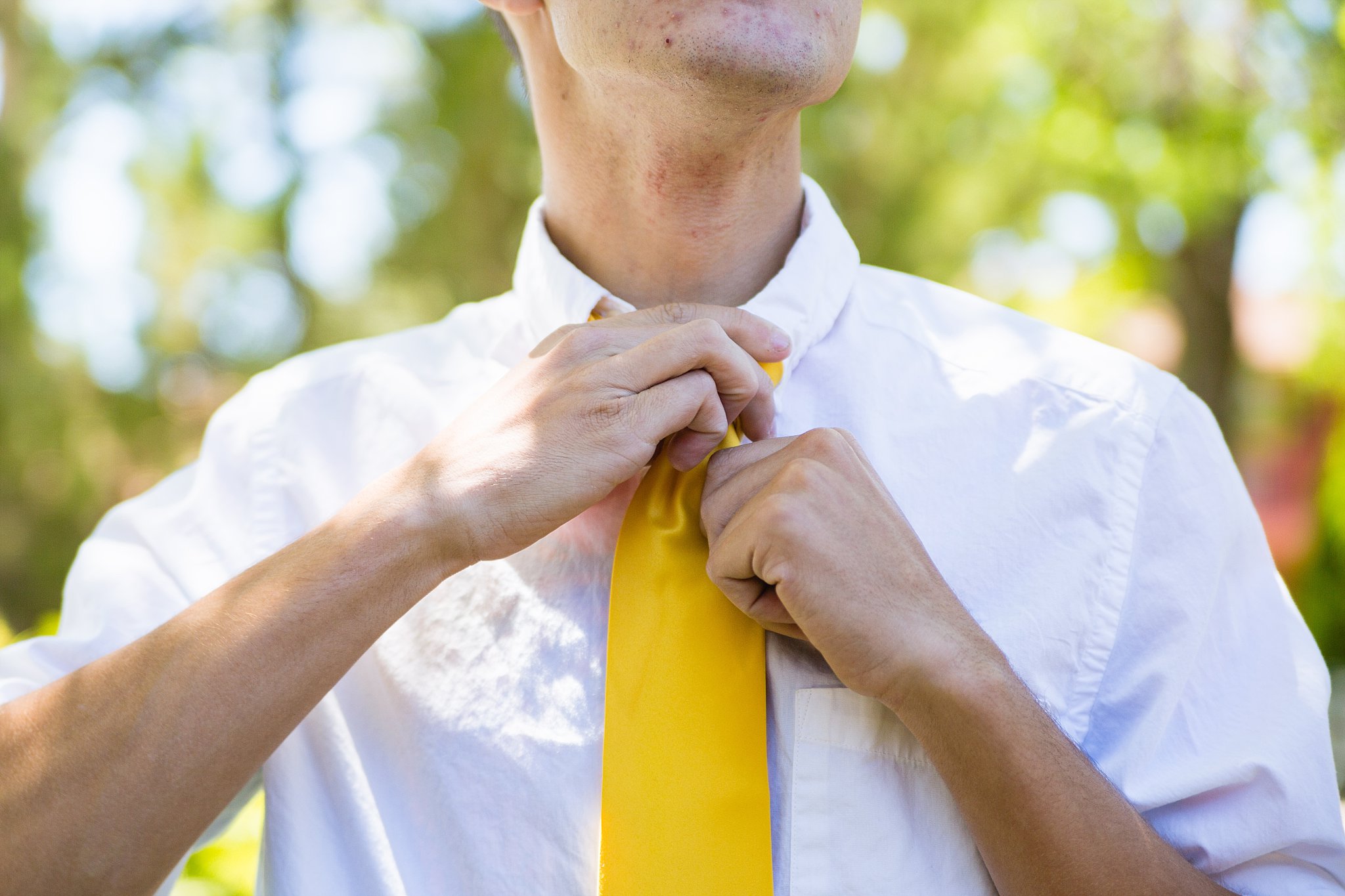 Groom adjusting his yellow tie while getting ready for his wedding by PMA Photography.