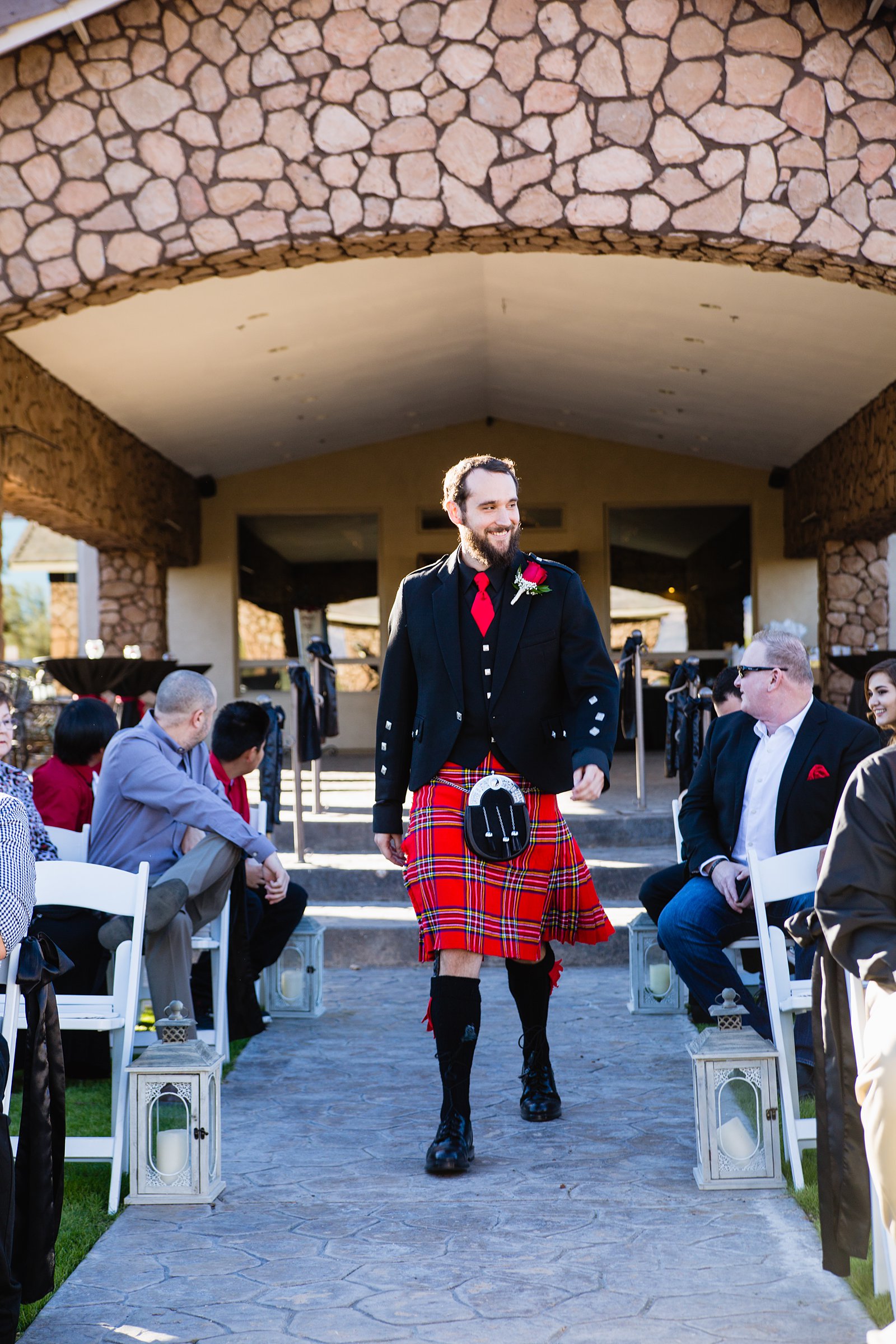 Scottish groom in red and black kilt walking down the aisle for his wedding ceremony by wedding photographers PMA Photography.