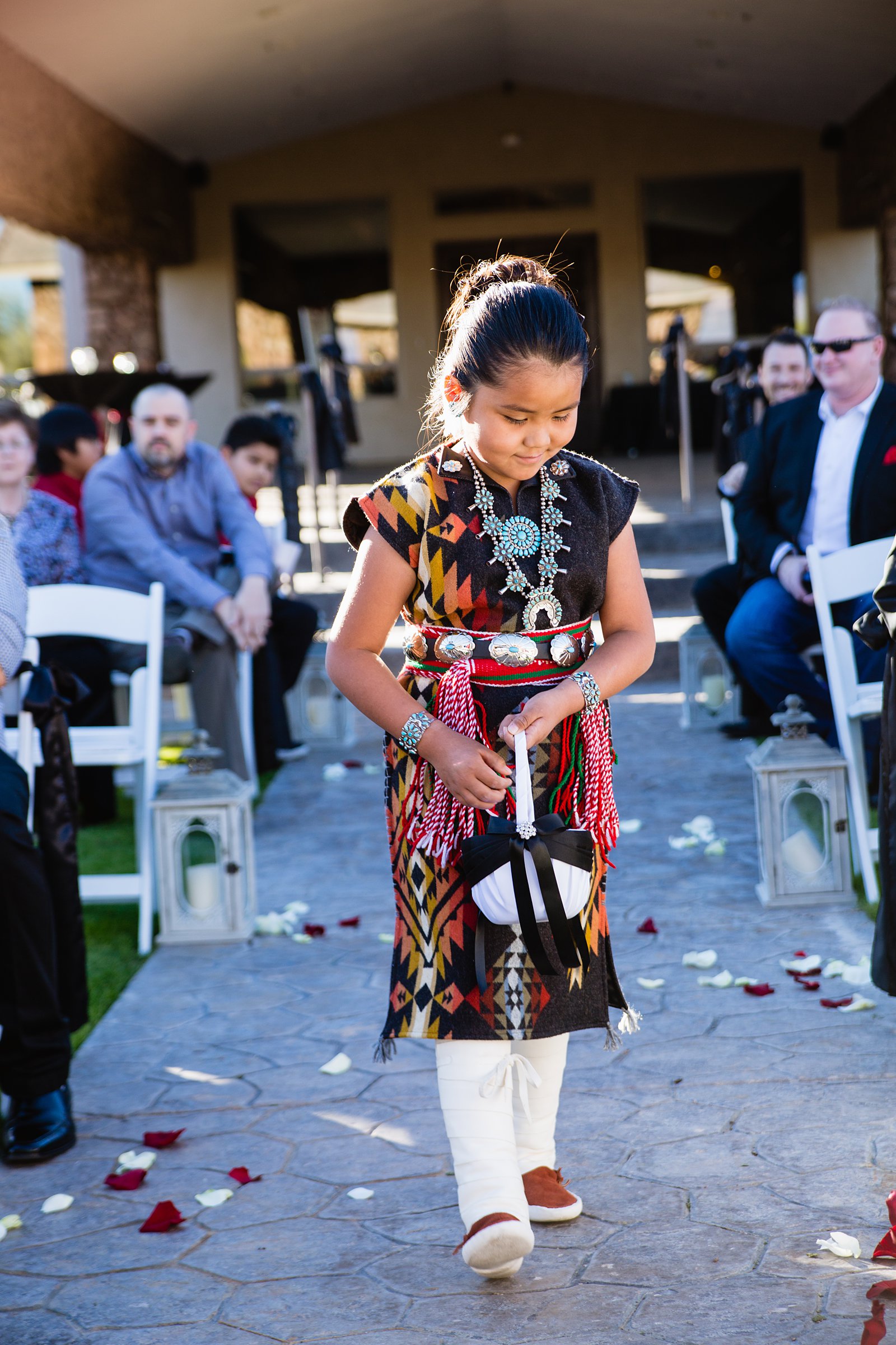 Flower girl in native outfit spreading pedals down the aisle by Arizona wedding photographer PMA Photography.