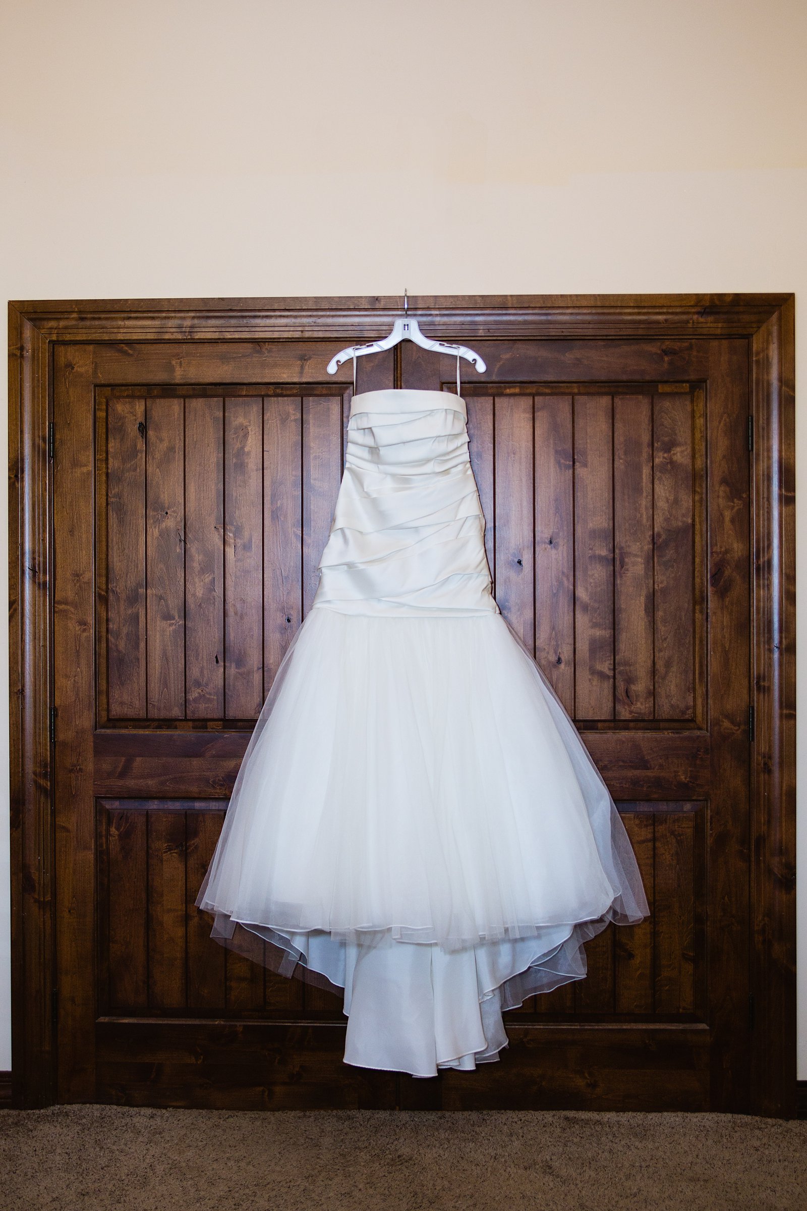 Brides simple classic wedding dress hanging from a door by PMA Photography.