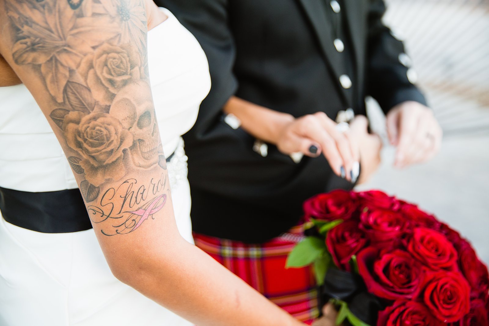 Tattooed bride holding a red rose bouquet by PMA Photography.