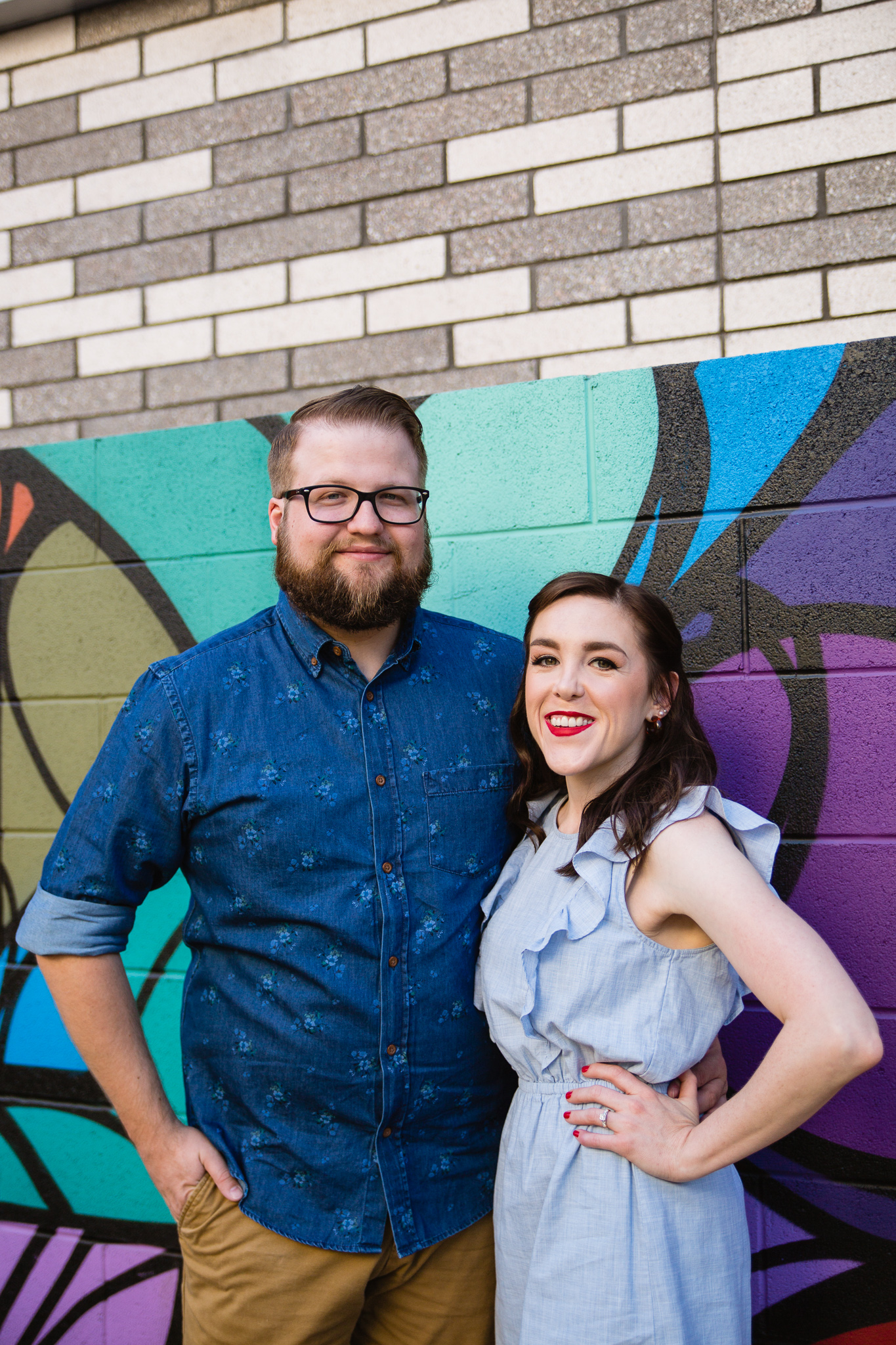 Couple pose in front of colorful mural in downtown Phoenix during their engagement session by PMA Photography.