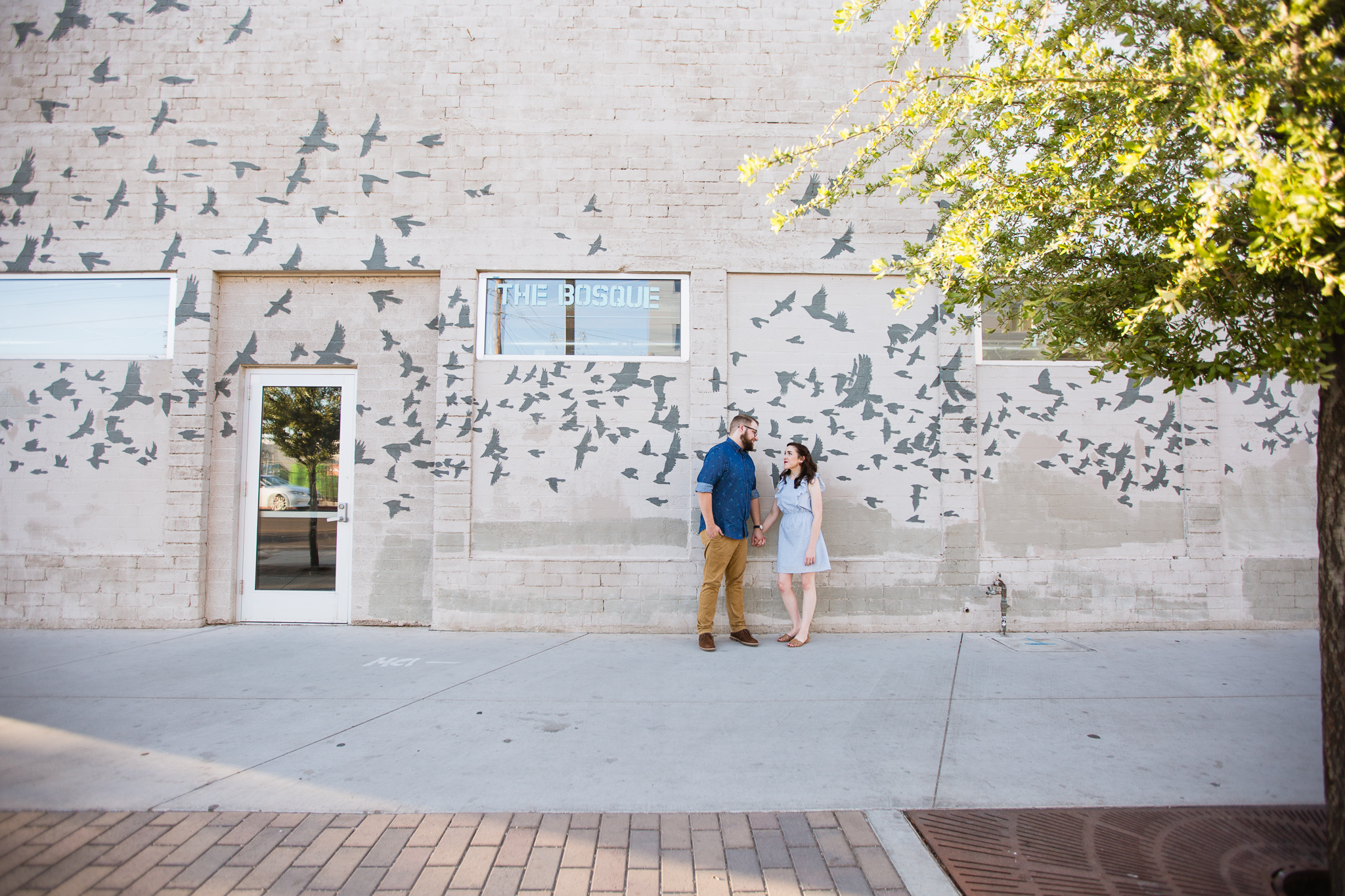 Couple looking at each other in front of a bird mural at Roosevelt Row during their downtown Phoenix engagement session by PMA Photography.