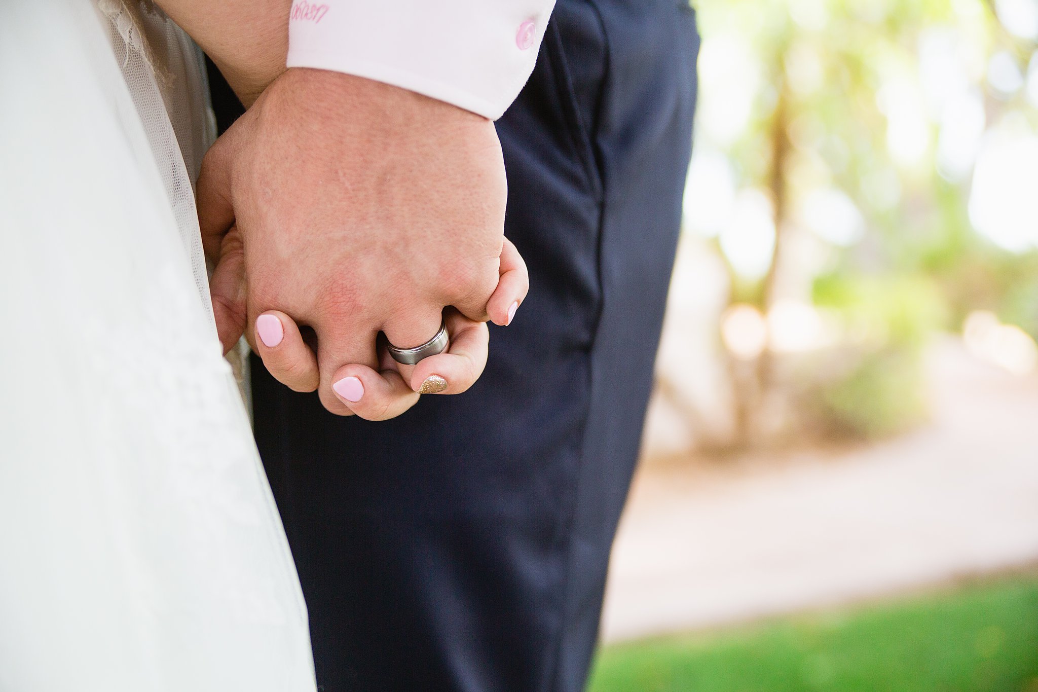 Grooms simple wedding band while holding hands with his bride by PMA Photography.