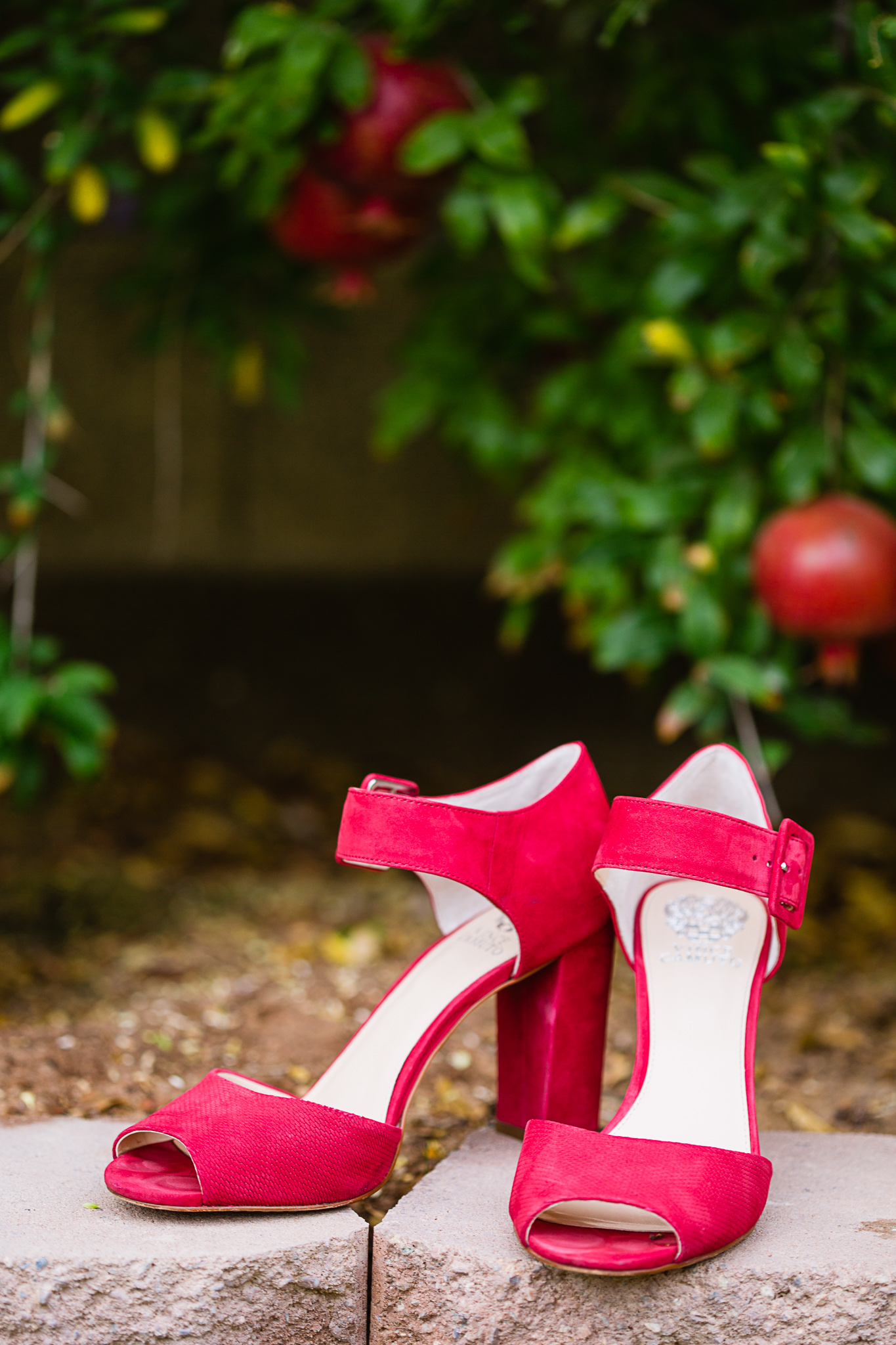 Detail image of bride's red wedding shoes in front of a pomegranate garden by Phoenix wedding photographer PMA Photography.