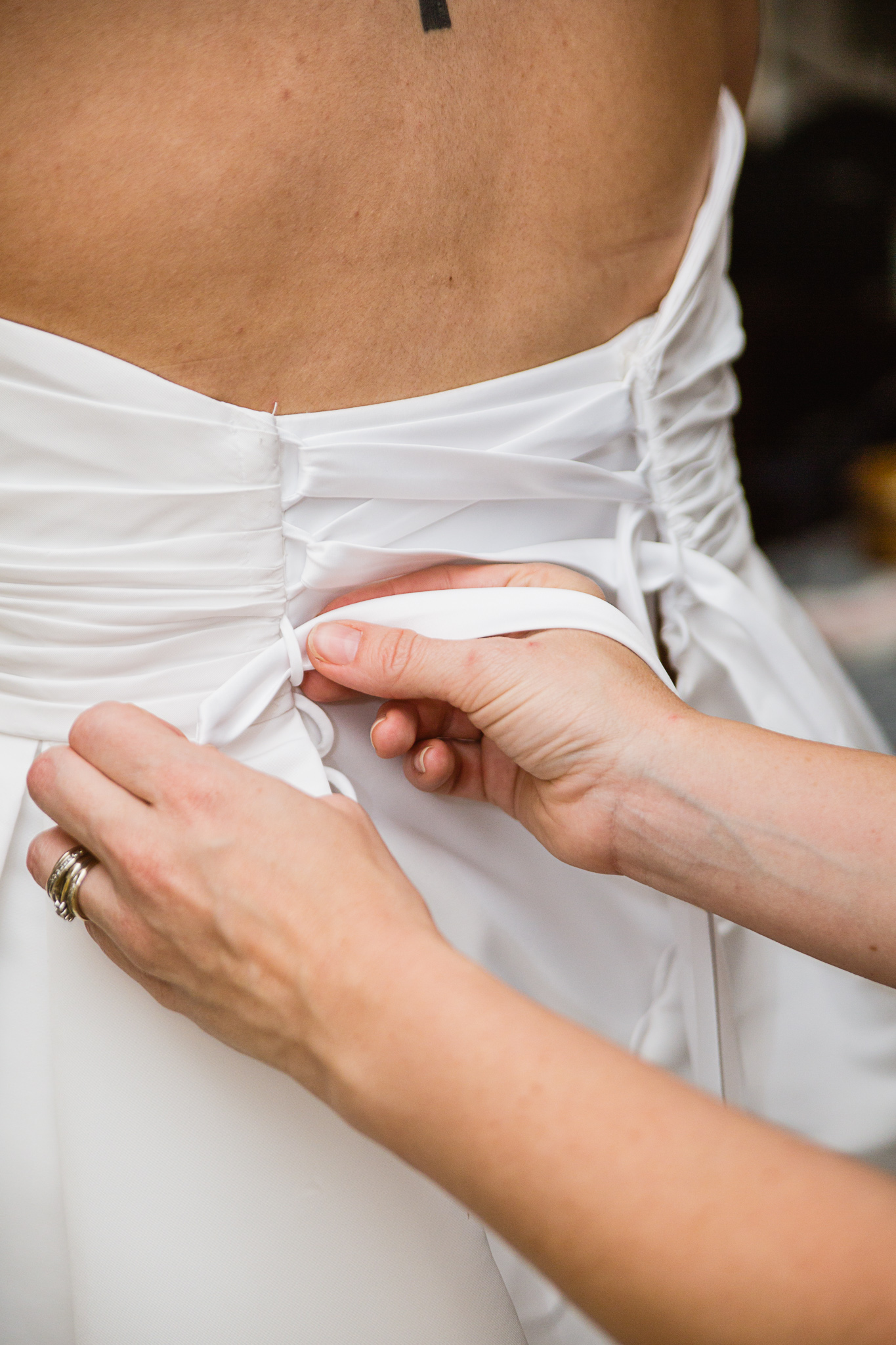 Bride's dress being laced up while getting ready for her wedding by photographer PMA Photography.