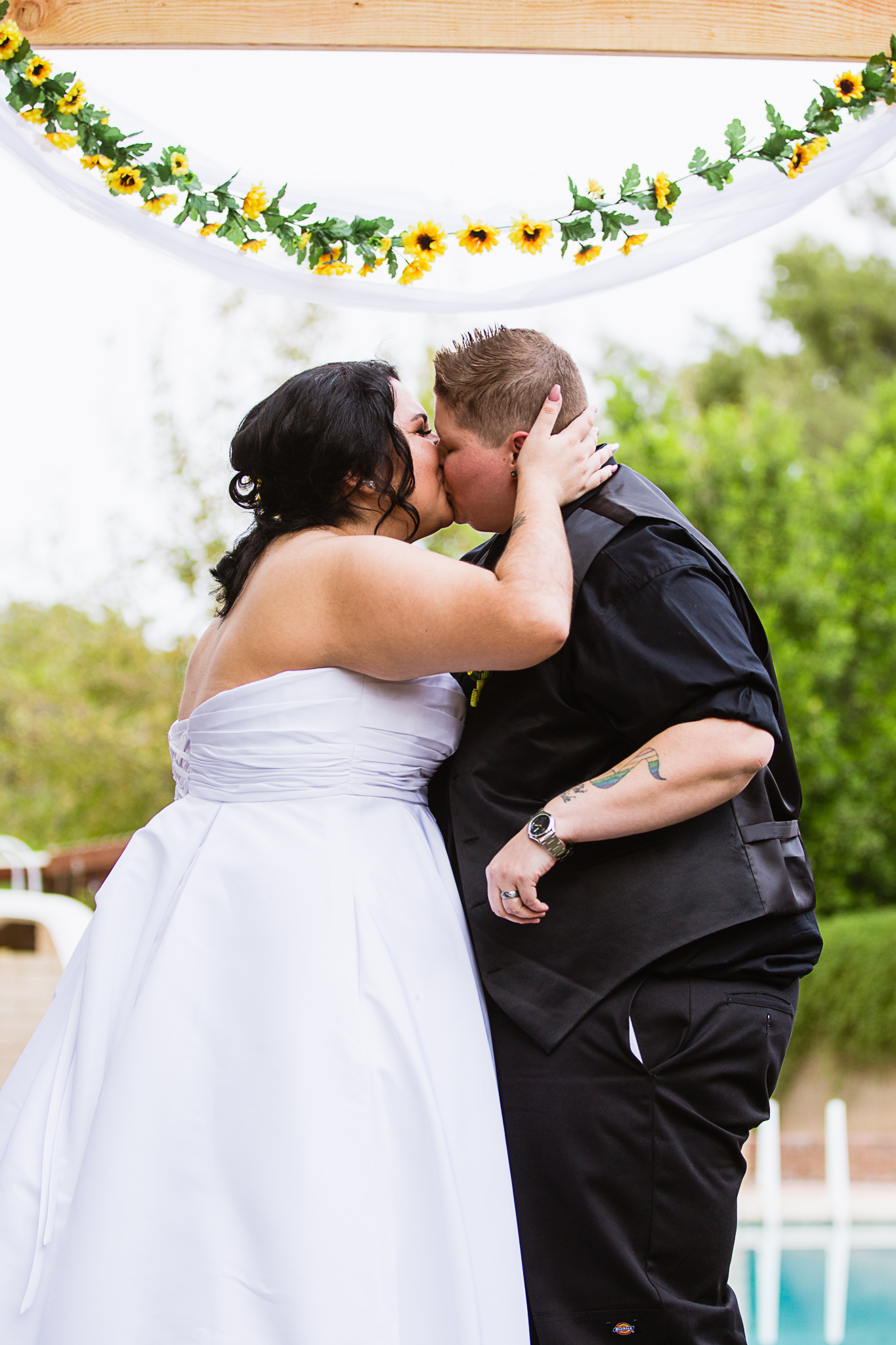 Brides kissing during LGBT backyard garden ceremony by Phoenix wedding photographer PMA Photography.