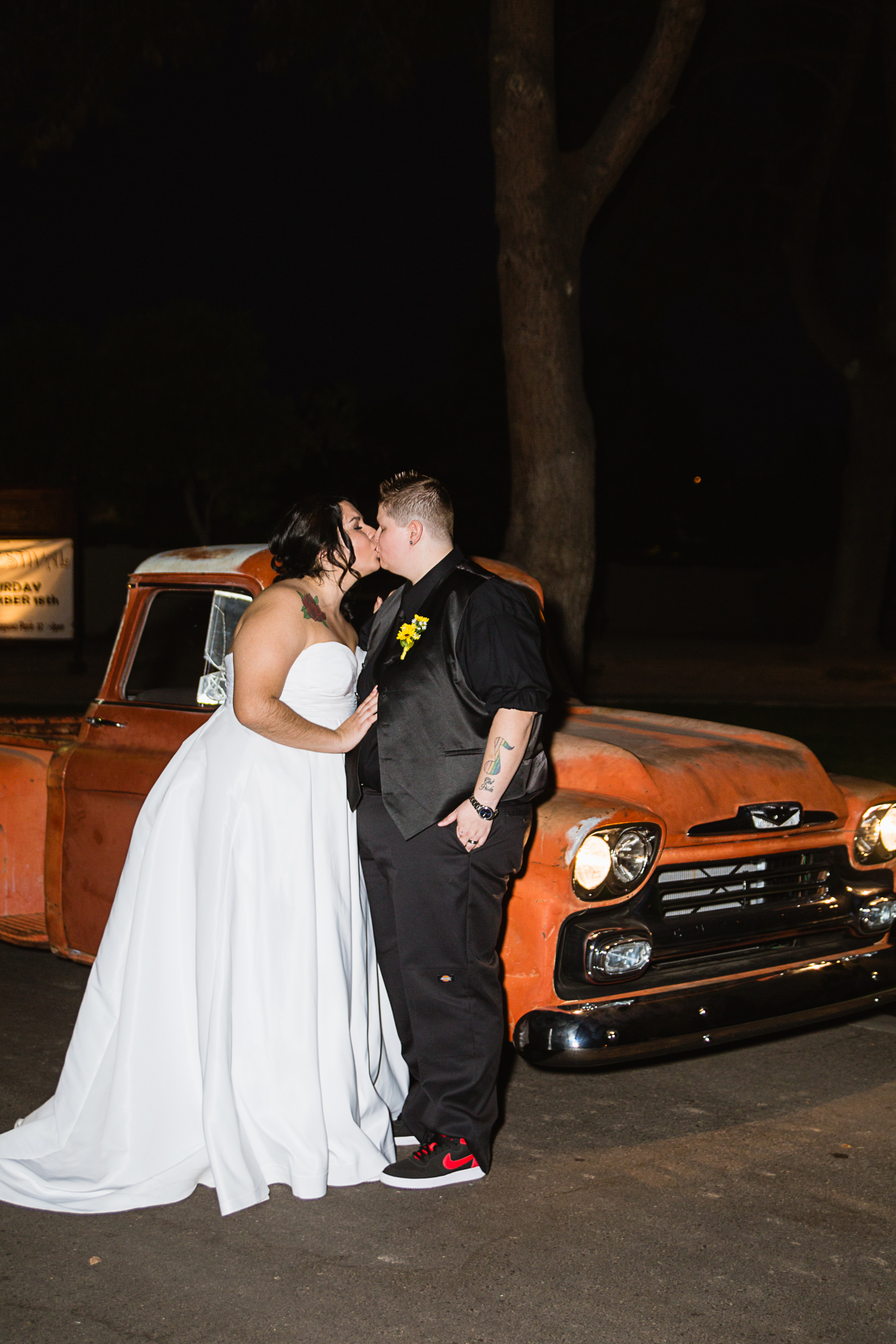 Same sex couple kissing at night in front of vintage orange truck.