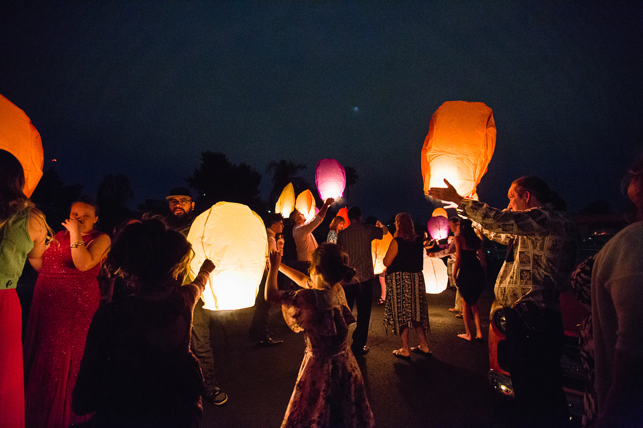 Guests light paper lanterns at wedding as part of their reception to remember lost loved ones by wedding photographer PMA Photography.