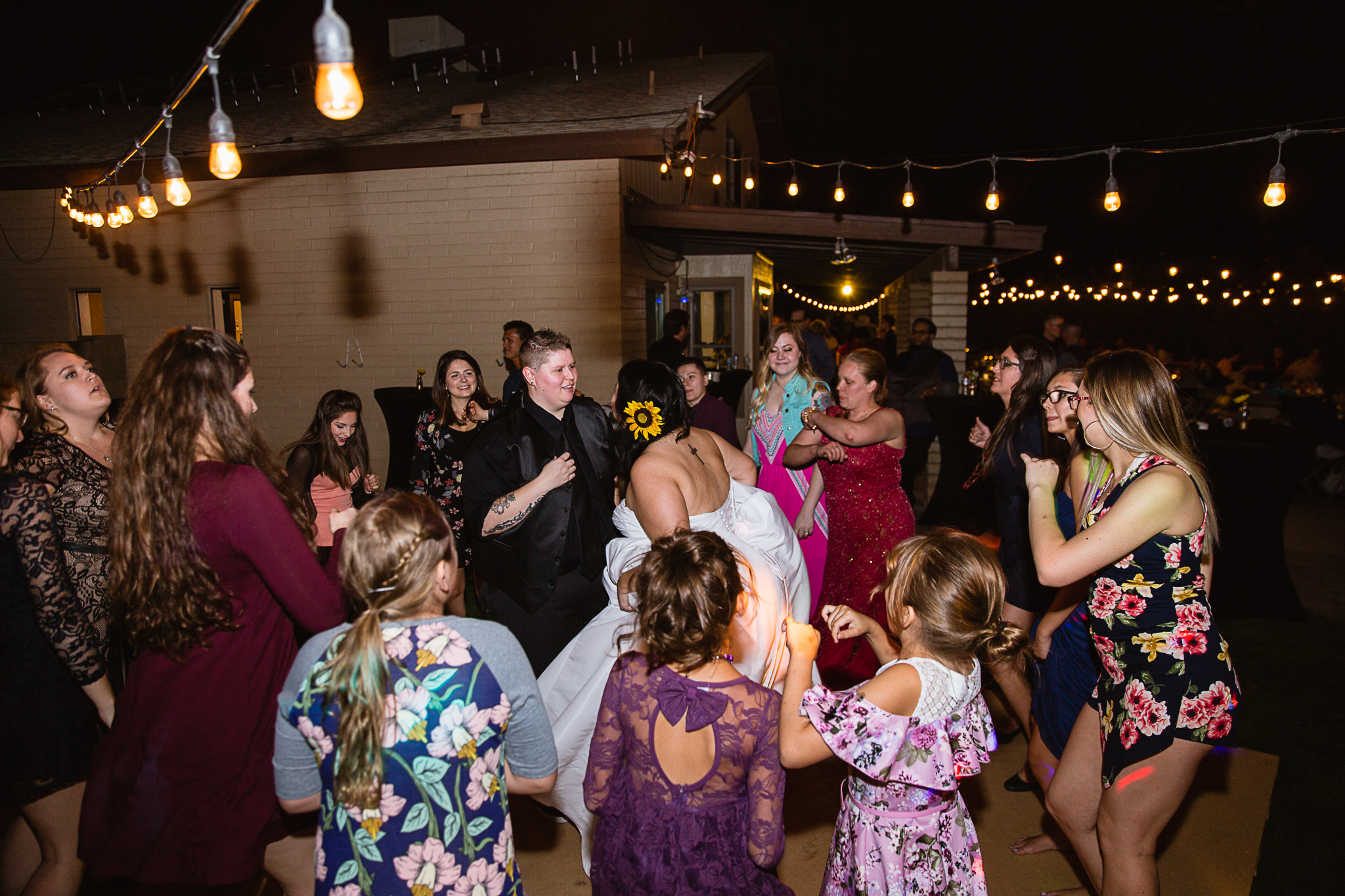 Brides dancing with guests at their backyard garden wedding reception by Phoenix wedding photographer PMA Photography.