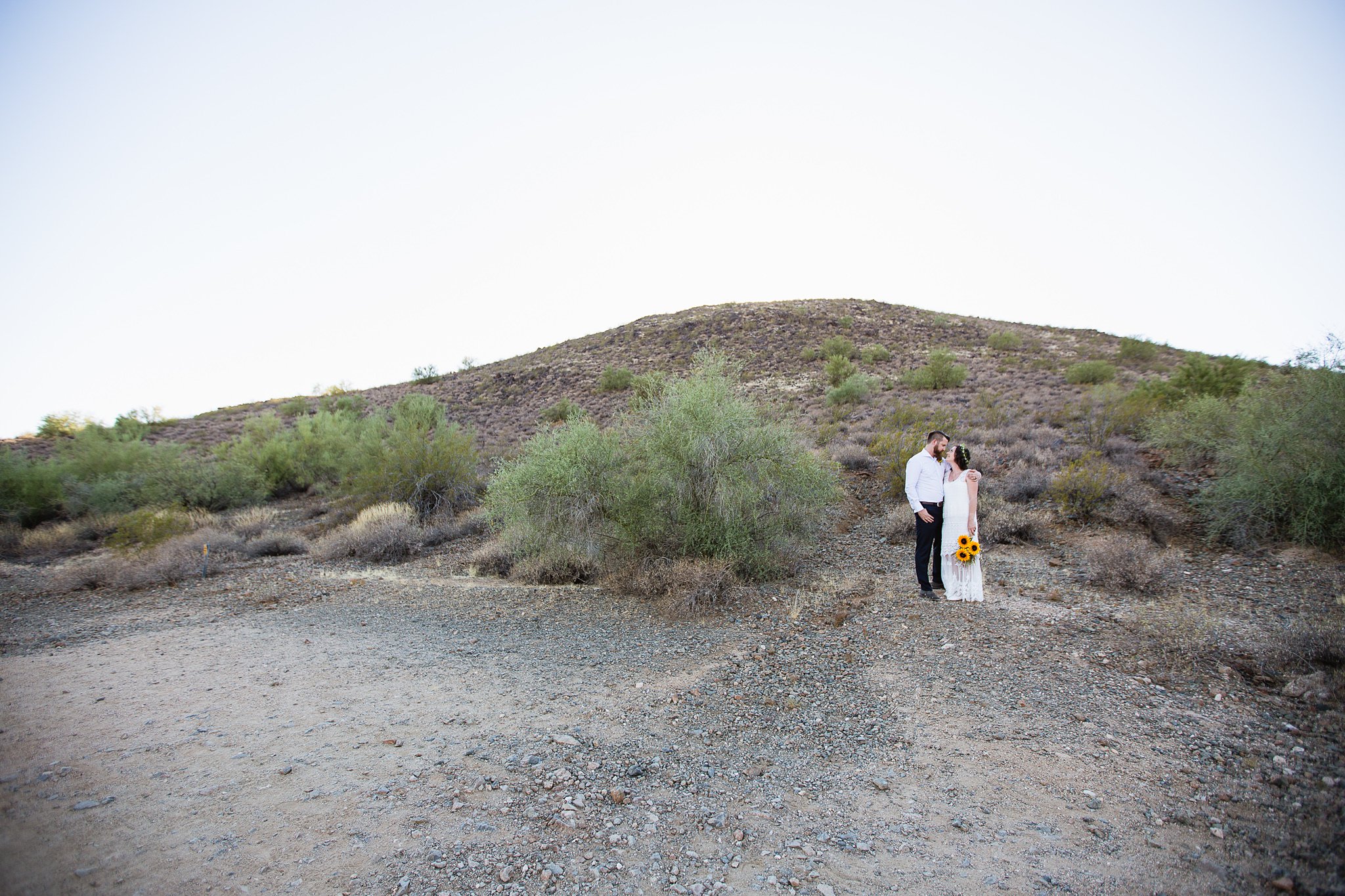 Simple boho inspired bride and groom look at each other in the desert by Arizona wedding photographers PMA Photography.
