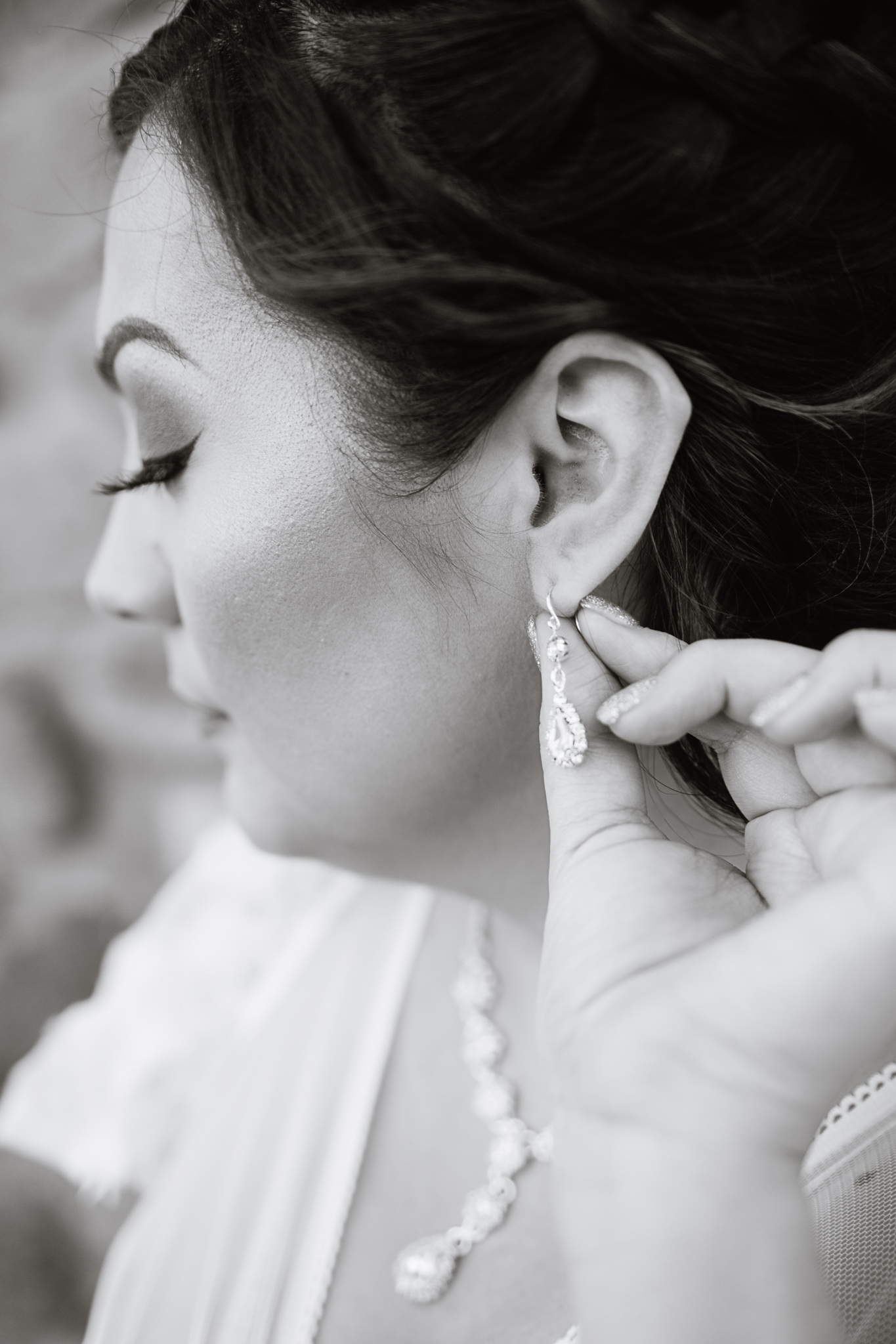 Black and white image of a bride adjusting her earrings while getting ready for her wedding by PMA Photography.