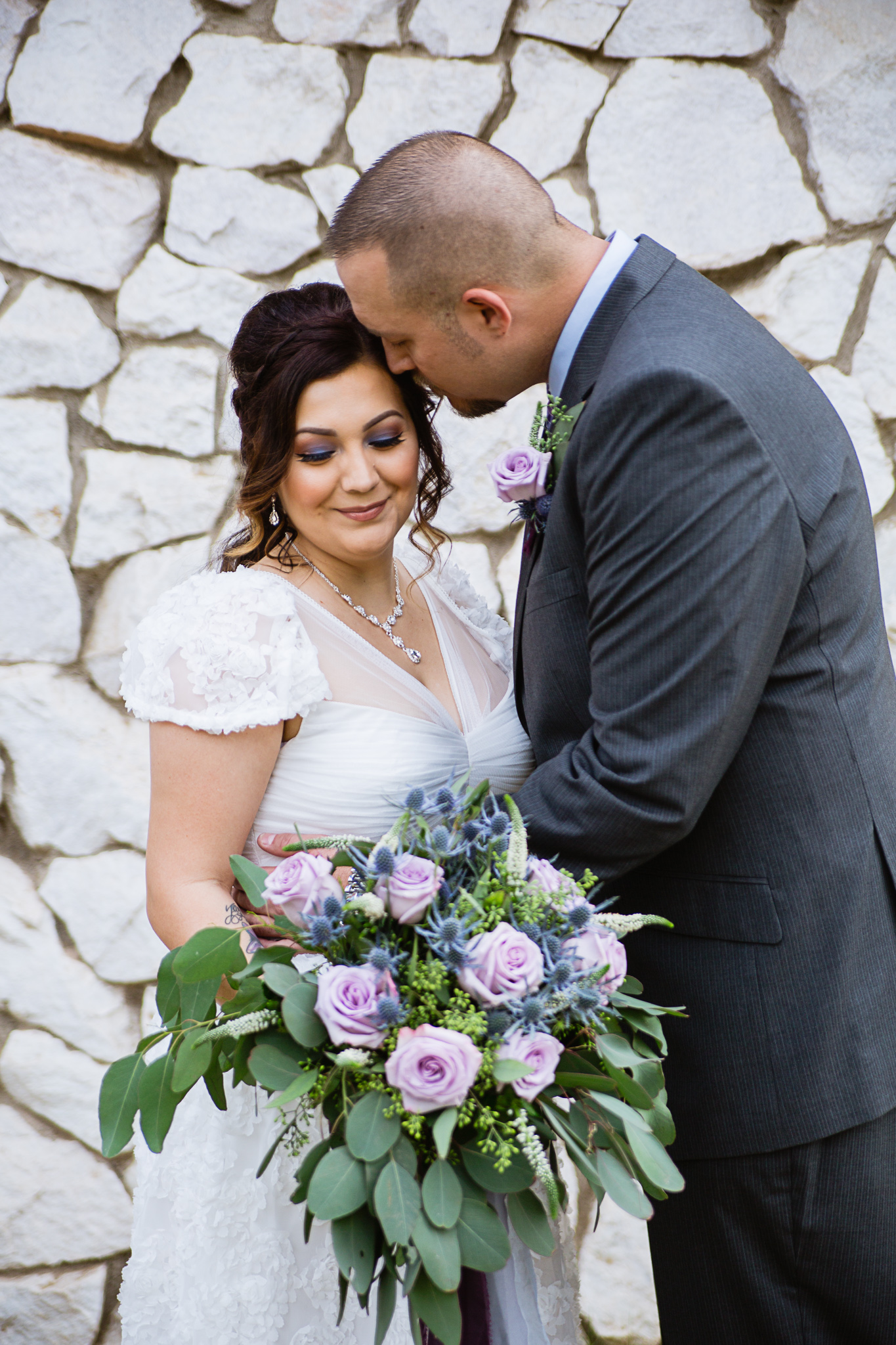 Bride and groom share an intimate moment while bride holds lavender and dusty blue bridal bouquet by PMA Photography.
