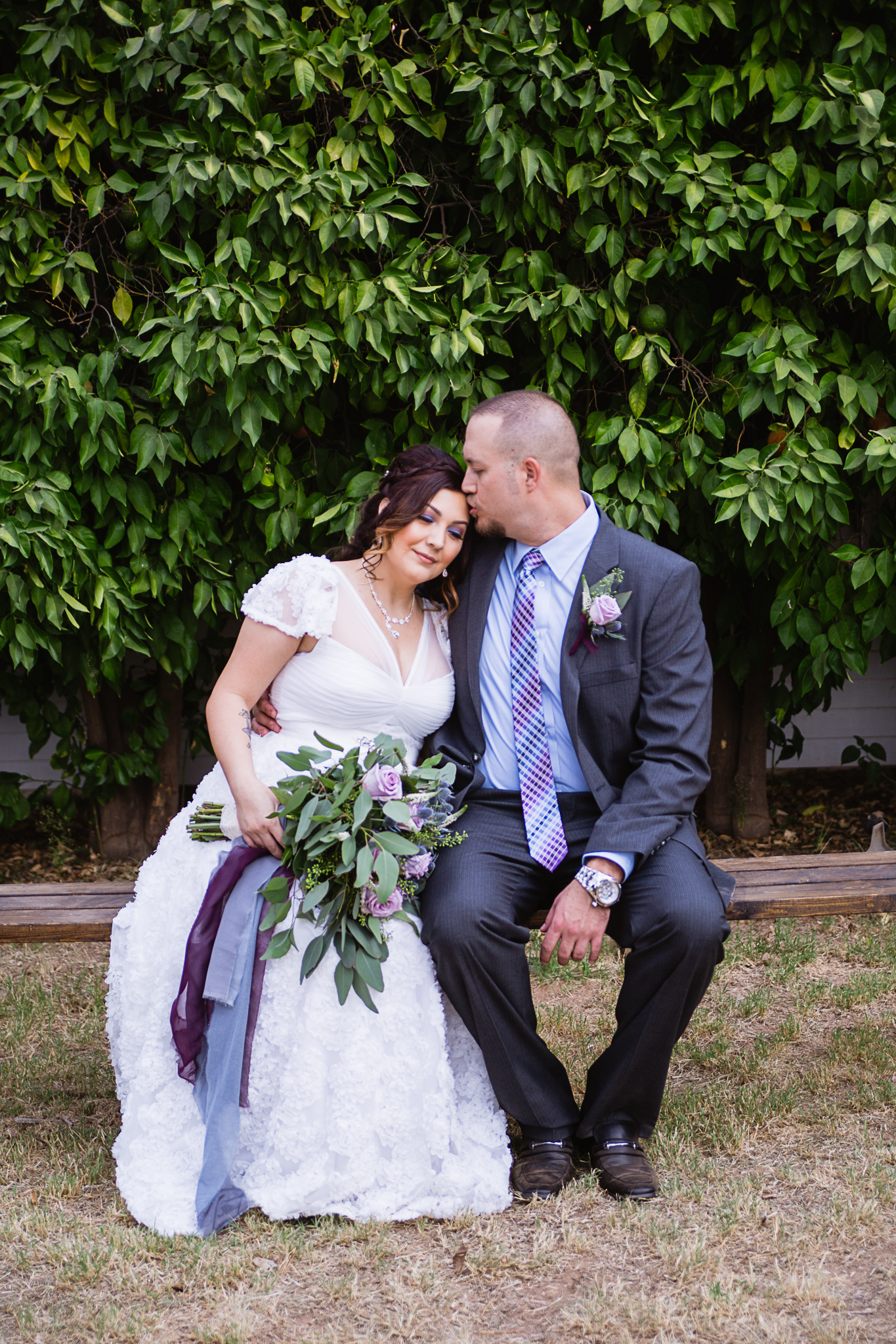 Groom kissing bride on the forehead at their Dusty Blue and Lavender backyard wedding by PMA Photography.