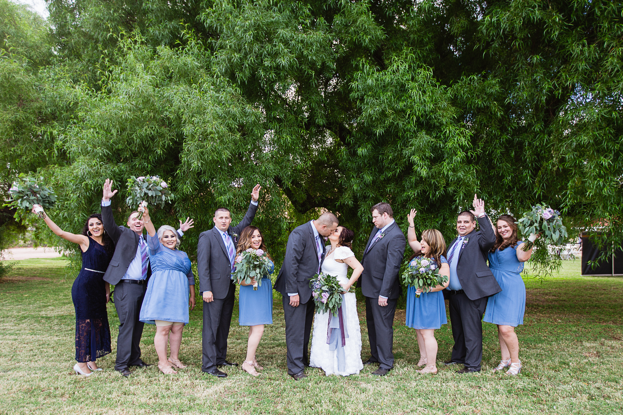 Bride and groom kiss as their bridal party reacts by PMA Photography.