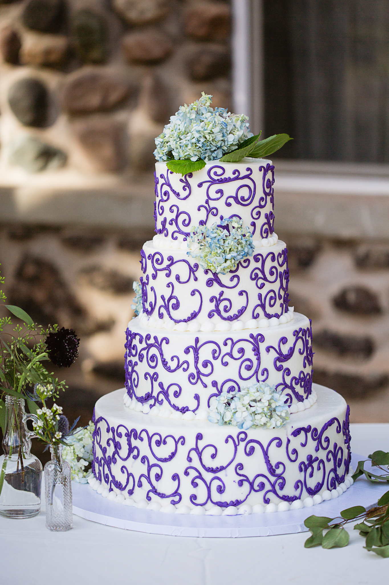 White and purple wedding cake decorated with blue hydrangea by PMA Photography.