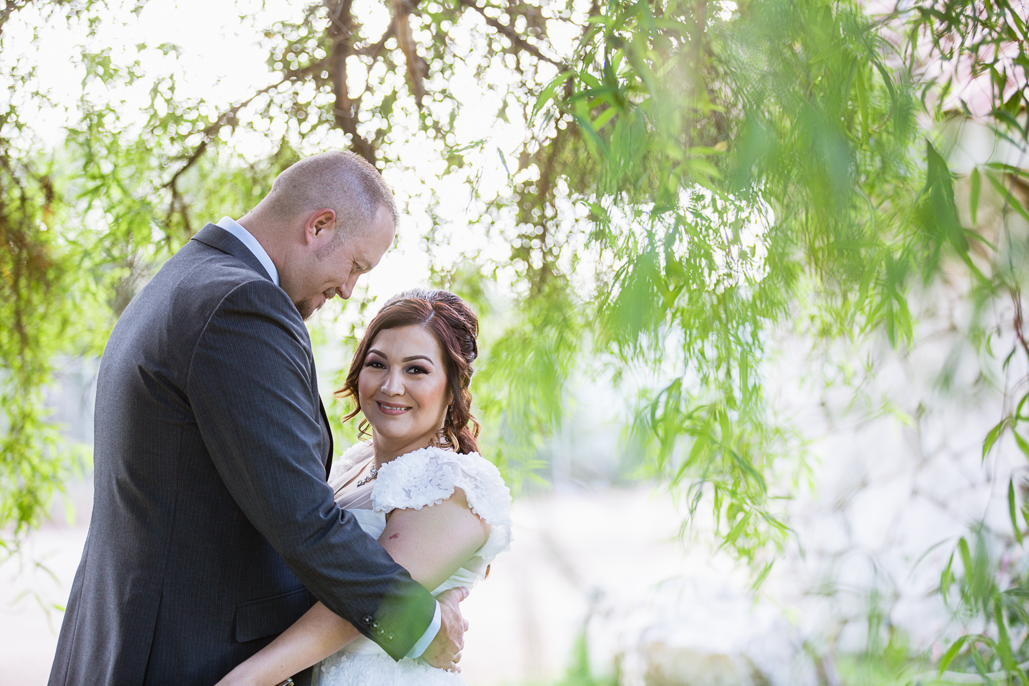 Groom looking at his bride under a willow tree on their wedding day by PMA Photography.