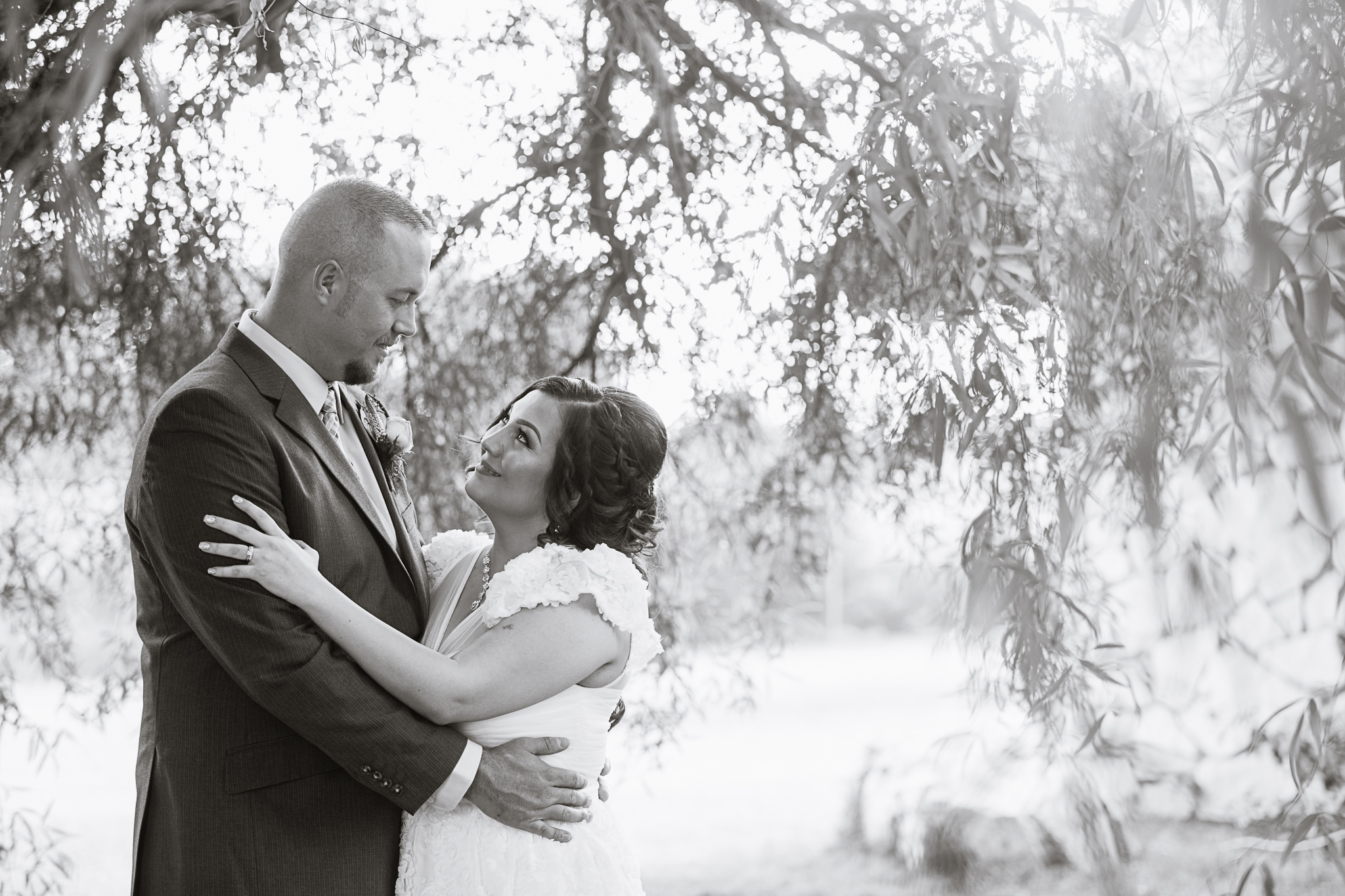 Black and white image of bride and groom looking at each other in a willow tree by PMA Photography.