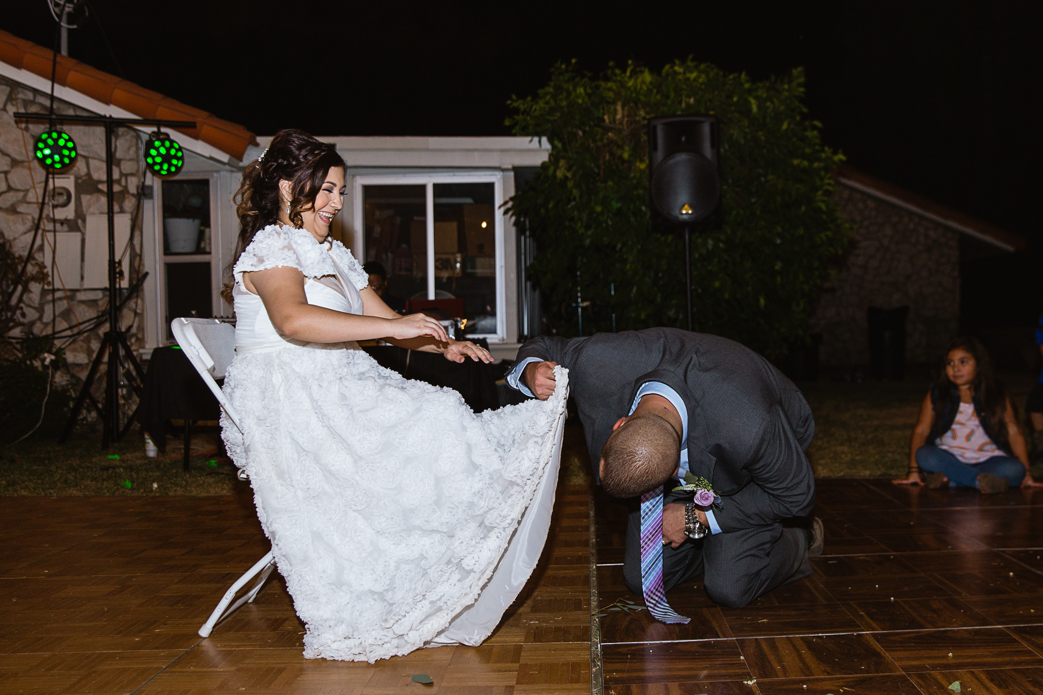 Bride laughs as groom goes under her dress to get the garter by PMA Photography.
