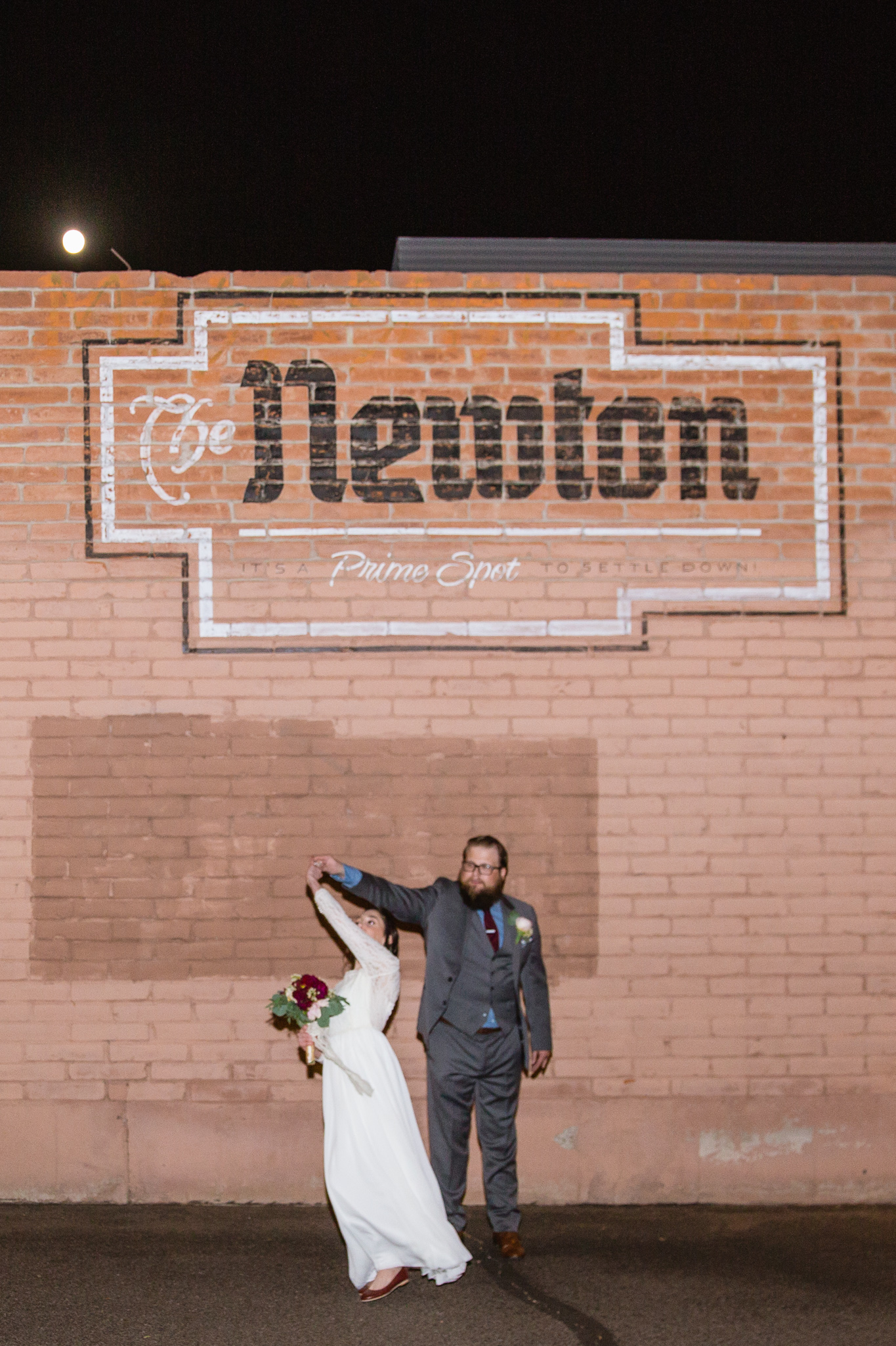 Bride and groom in from of The Newton sign on a brick wall outside of the venue where they were married.