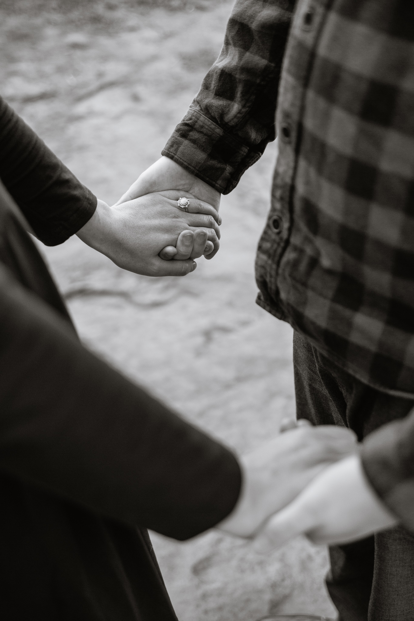 Black and white photo of couple holding hands focused on her engagement ring by PMA Photography.