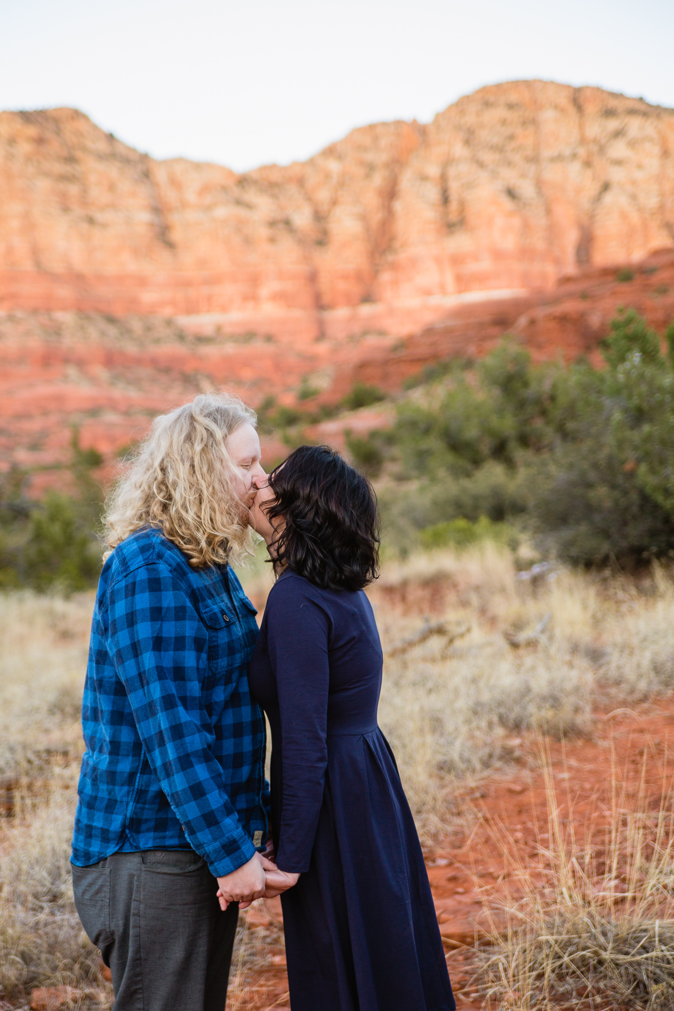 Couple holding hands and kissing during engagement session in Sedona Arizona by PMA Photography.