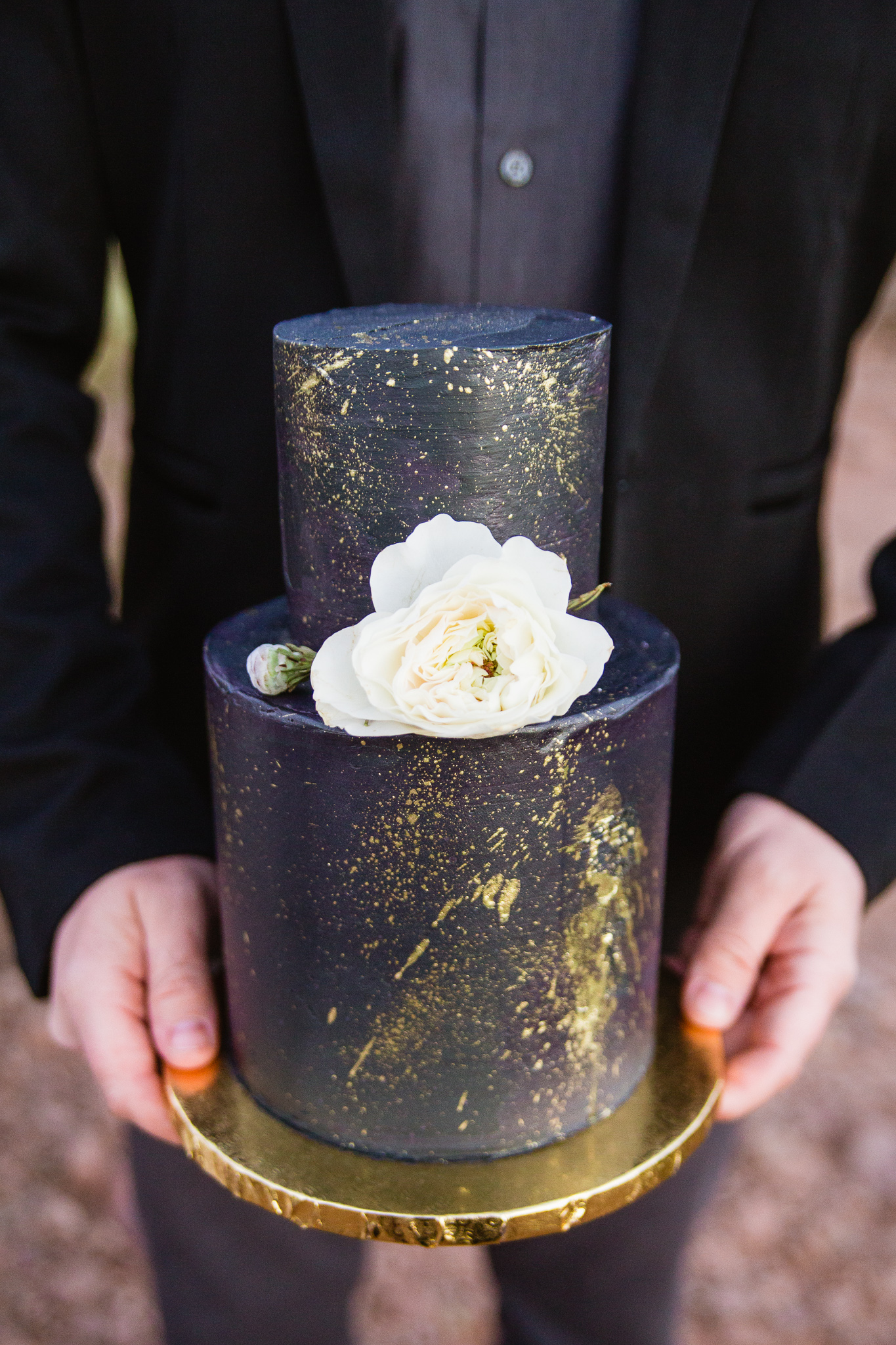 Wedding detail photograph of groom holding black white and gold small wedding cake for intimate wedding.