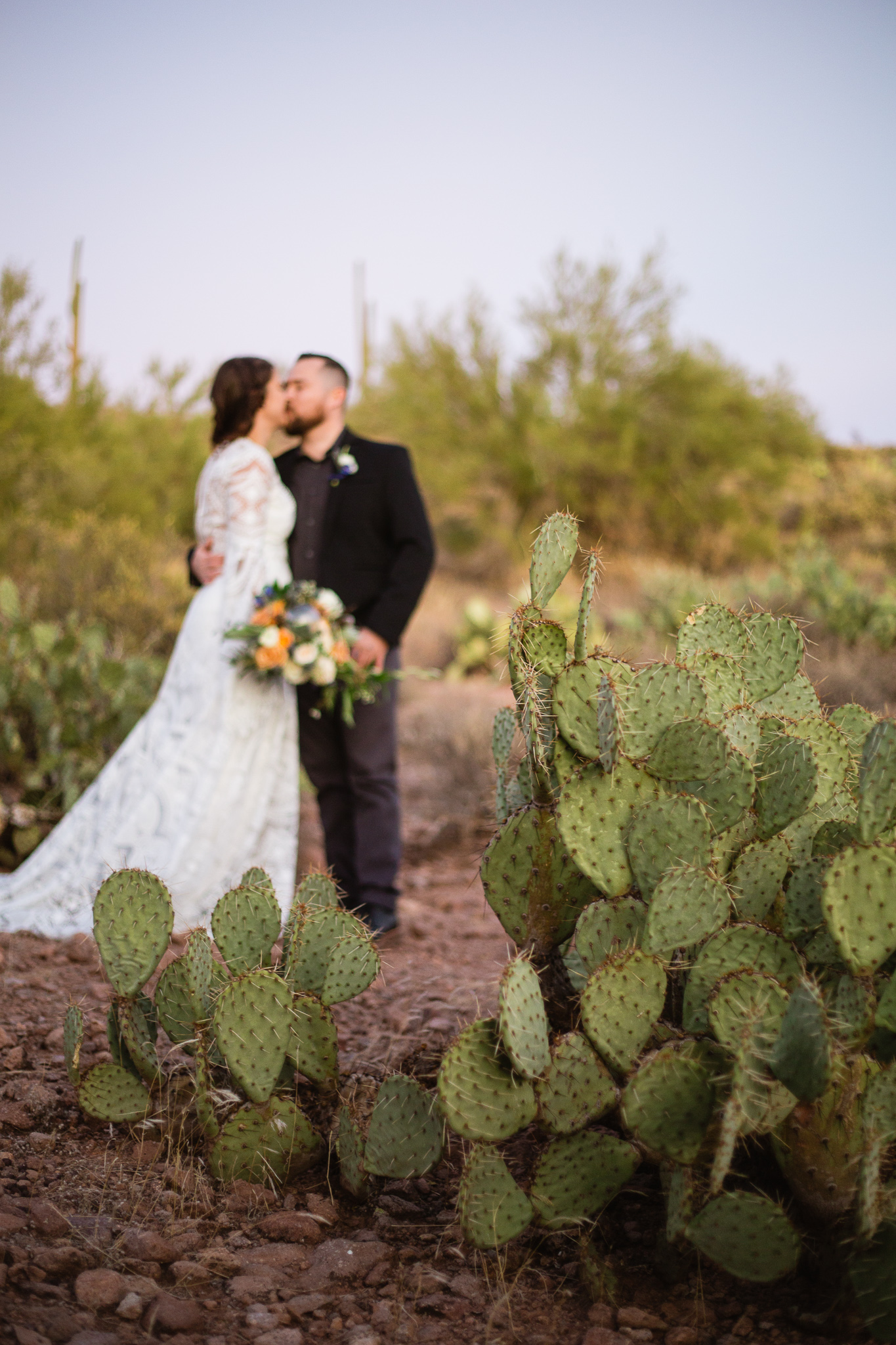 Witchy bohemian black white and gold inspired bride and groom at a Superstition Mountains styled wedding blurred in the background of an Arizona cactus.