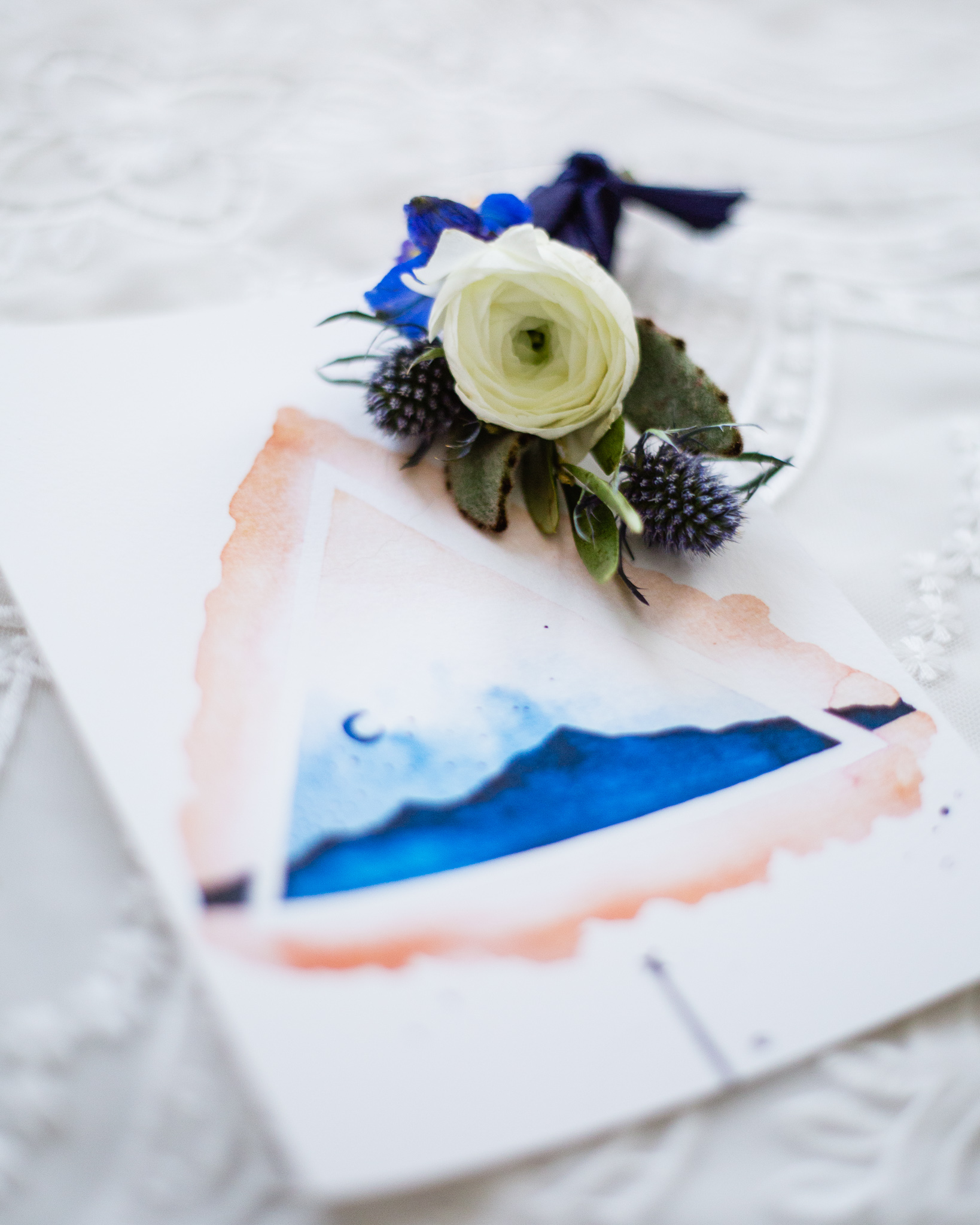 White blue and sage groom's wedding boutonniere with blue mountain inspired wedding invitation.