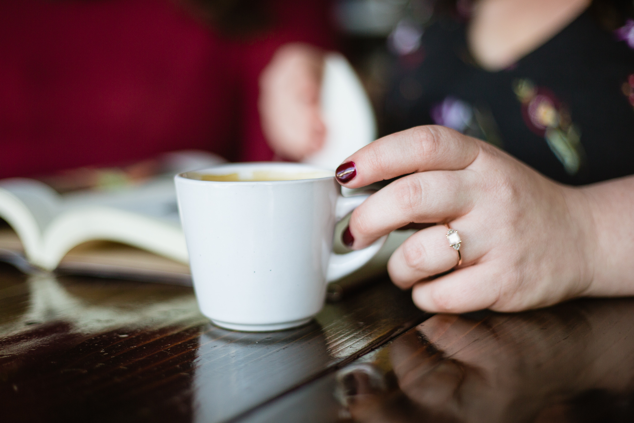 Close up image of a hand touching a coffee cup with an engagement ring.