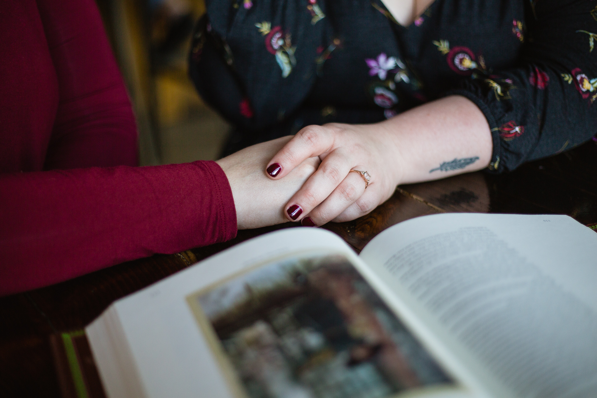 Couple holding hands next to book during engagement session at coffee shop.