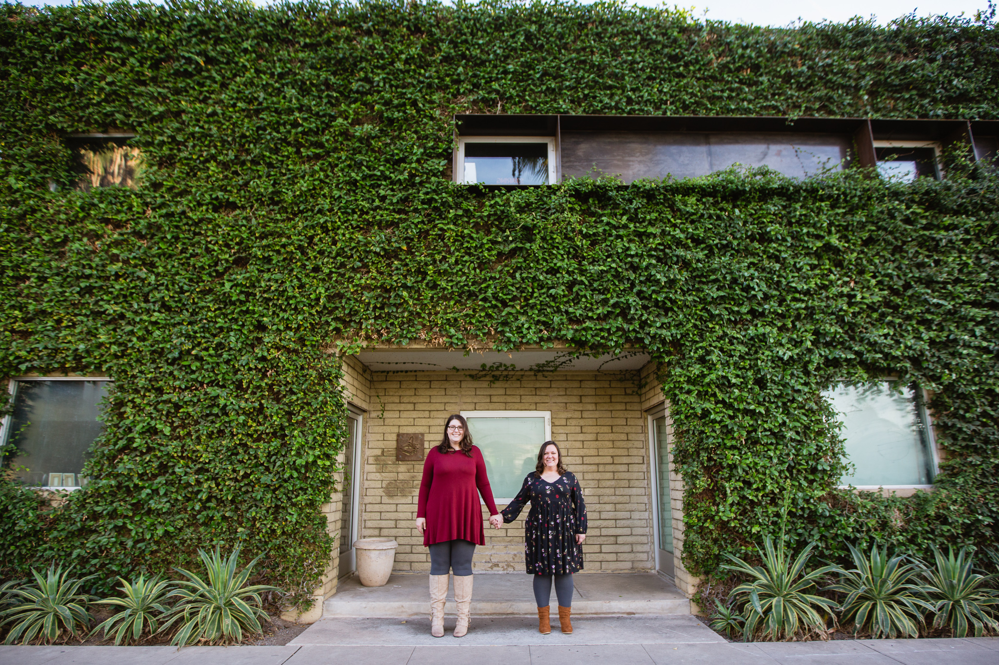 Couple standing in front of building covered in green ivy during their engagement session.