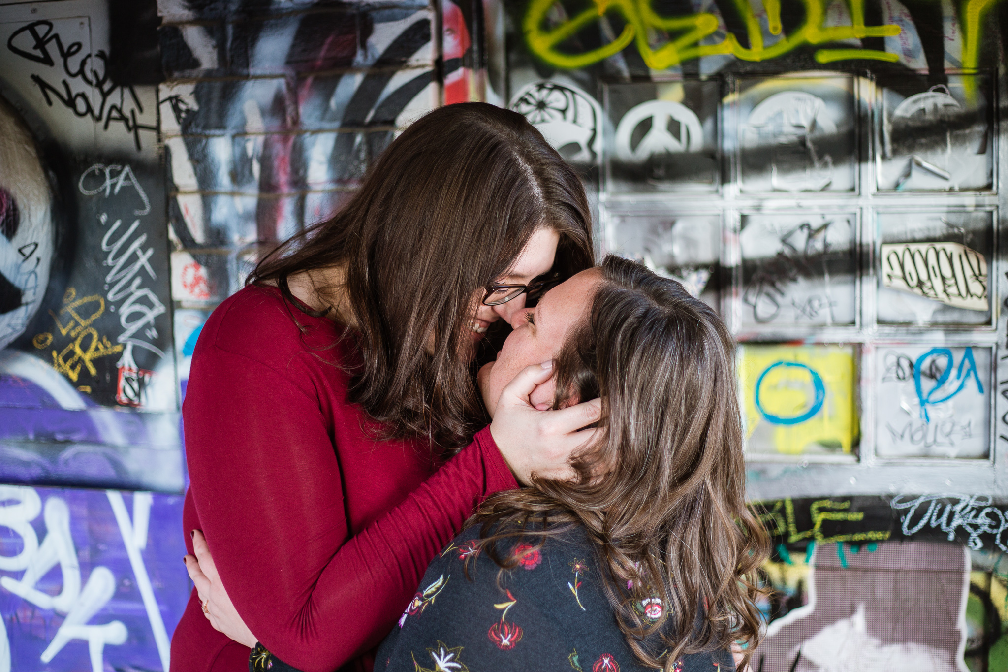 LGBT couple standing in front of a building covered in graffiti for their engagement photos on Roosevelt Row.