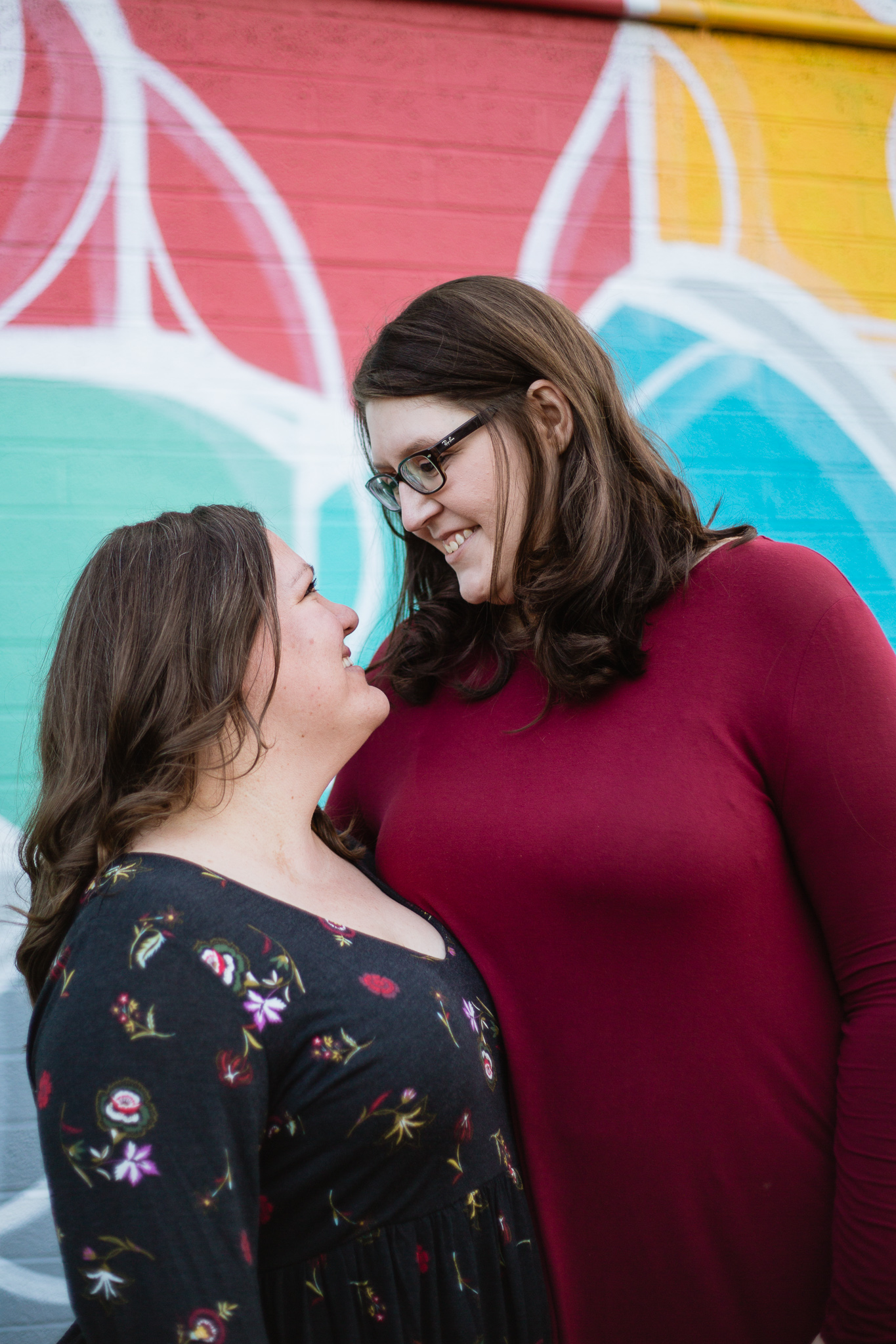 LGBT couple laughing together in front of a mural for their engagement photography session in downtown Phoenix at Roosevelt Row.