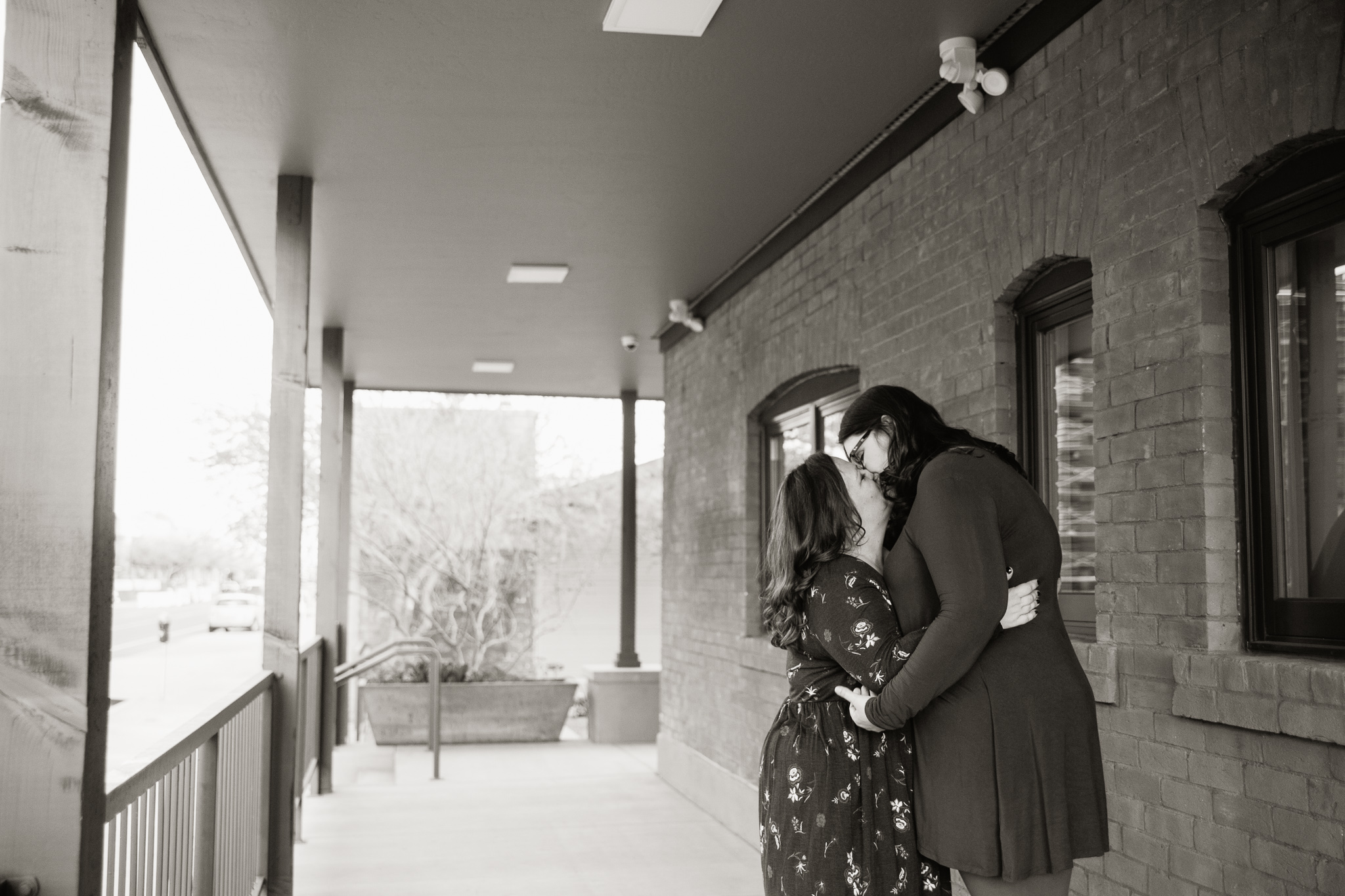 Black and white image of couple kissing on the porch of a brick house in downtown Phoenix.