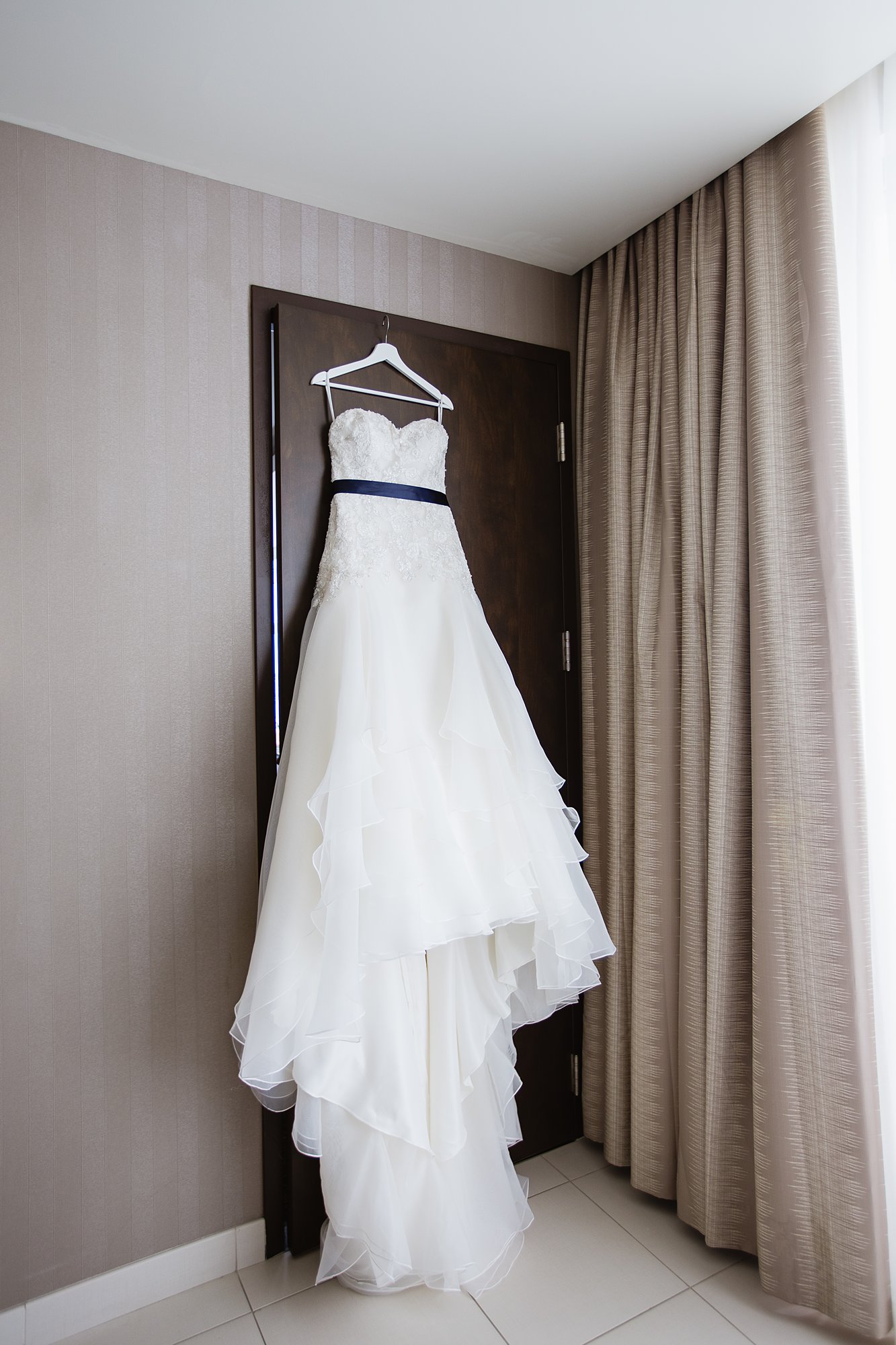 Bride's simple white dress hanging in hotel room.