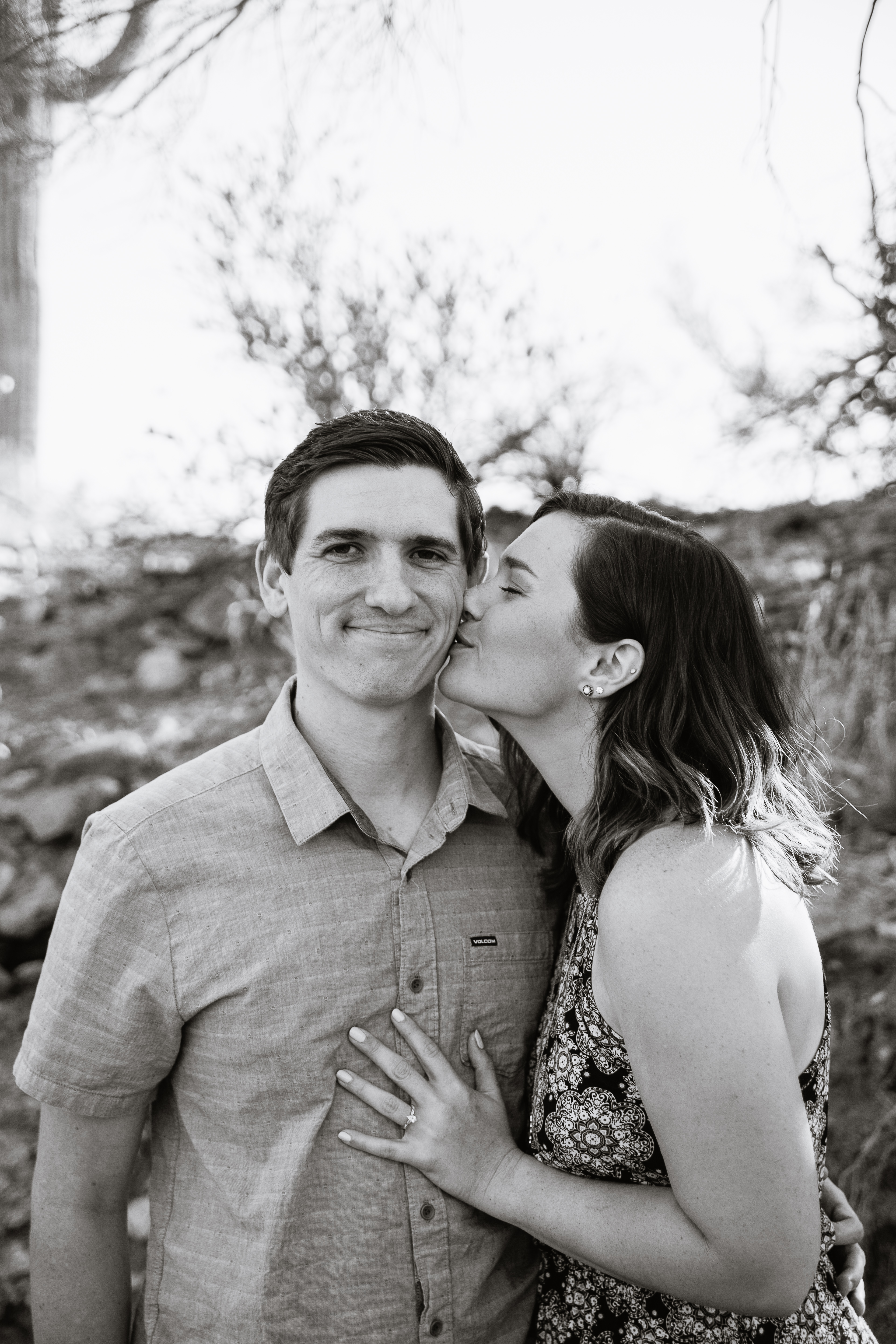 Black and white image of girl kissing fiance's cheek during their engagement session at Lost Dutchman State Park by engagement photographer PMA Photography.