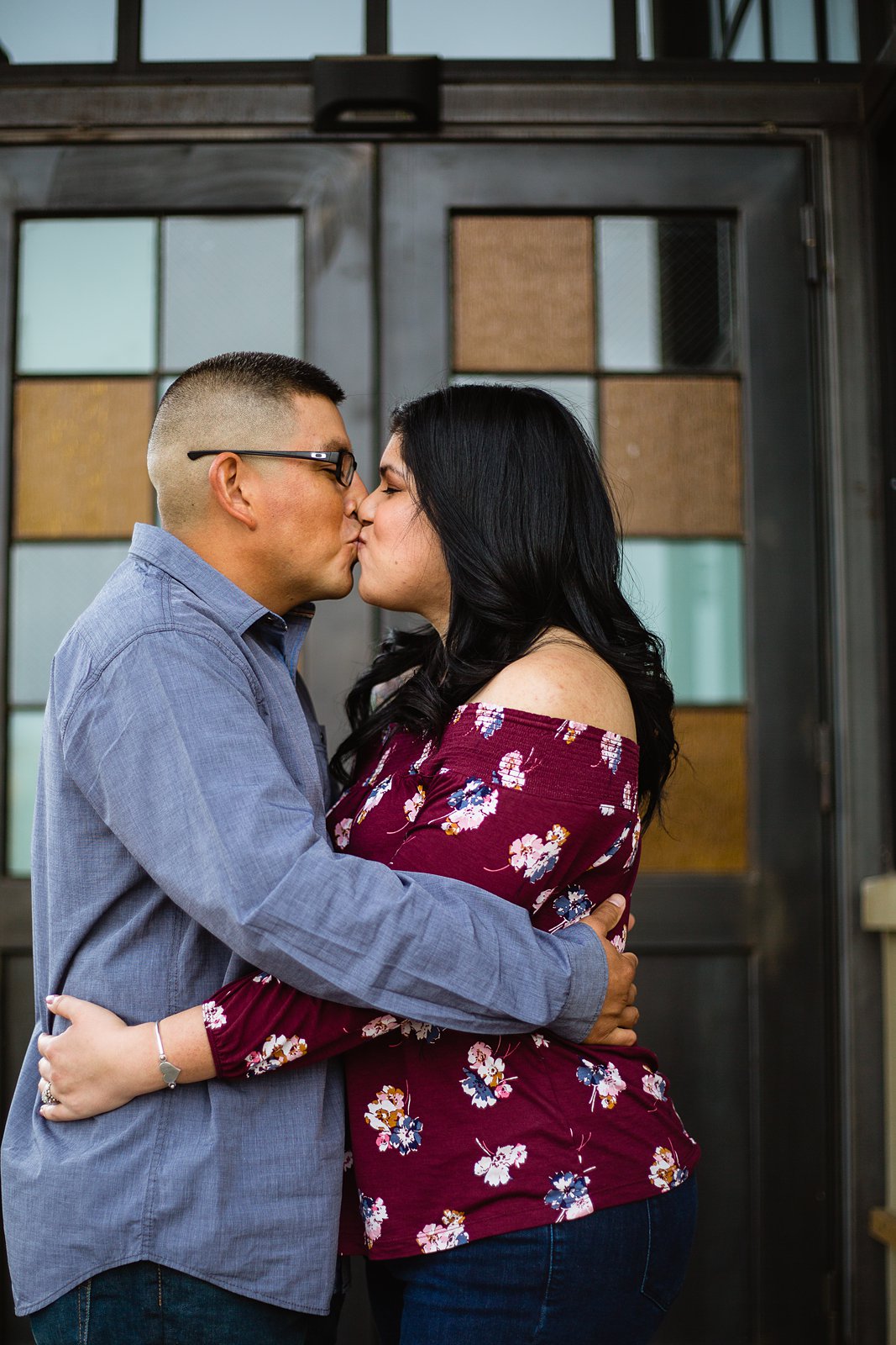 Couple kissing in front of checkered door during their Gilbert engagement session by PMA Photography.