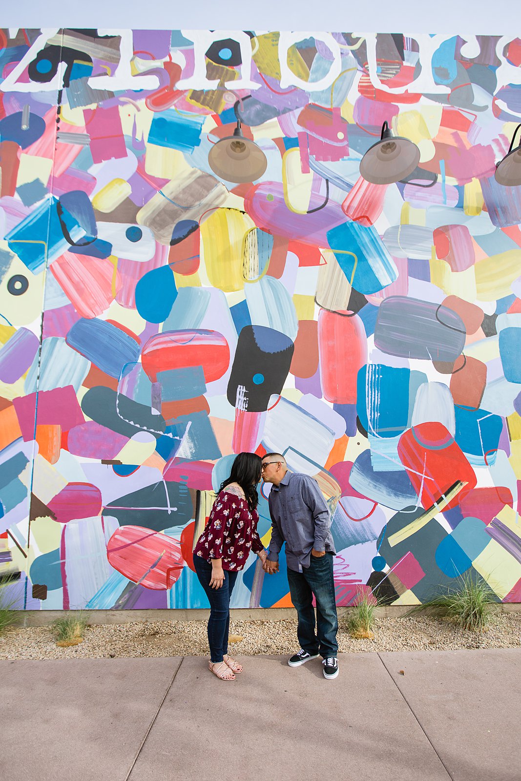 Couple in front of colorful art mural at their Gilbert heritage district engagement session by Arizona wedding photographers PMA Photography.