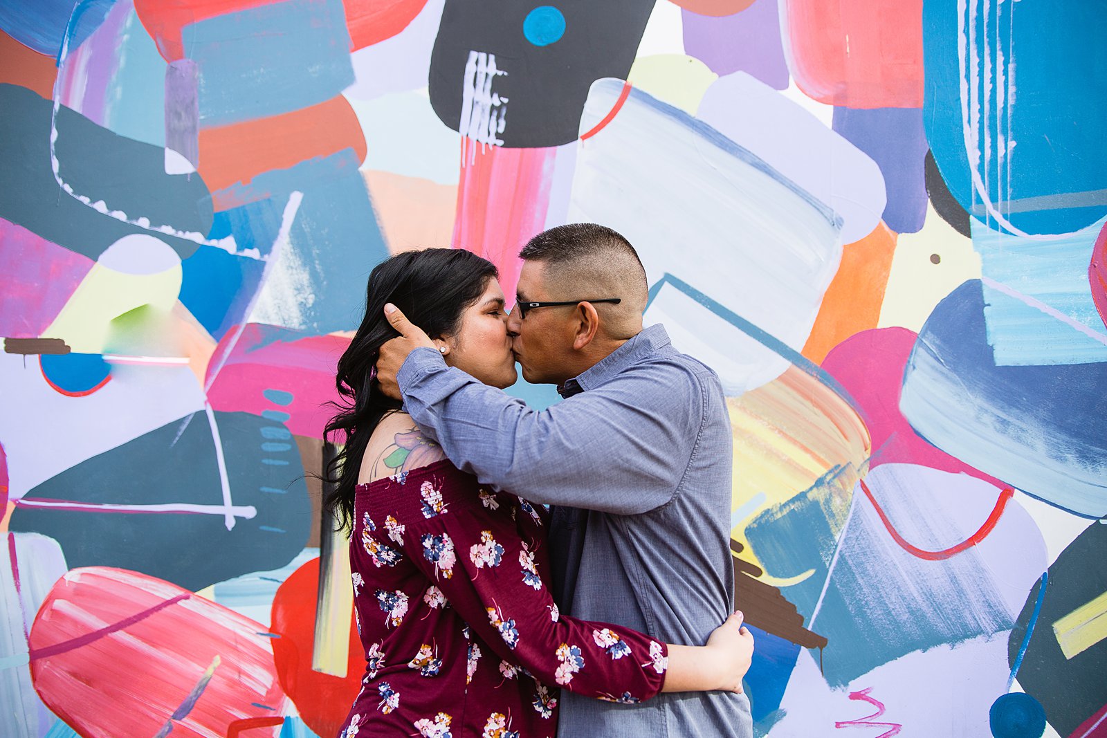 Couple kissing in front of colorful art mural at their Gilbert heritage district engagement session by Arizona wedding photographers PMA Photography.