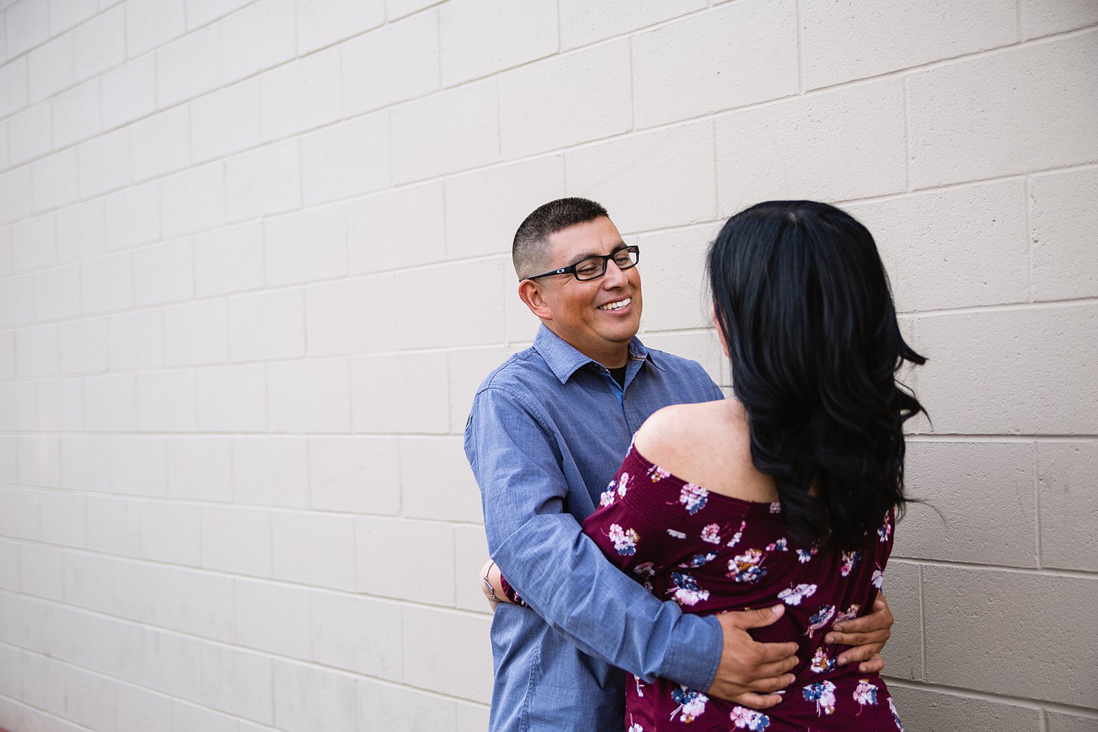 Couple looking at each other against brick wall during their engagement session by Phoenix wedding photographer PMA Photography.