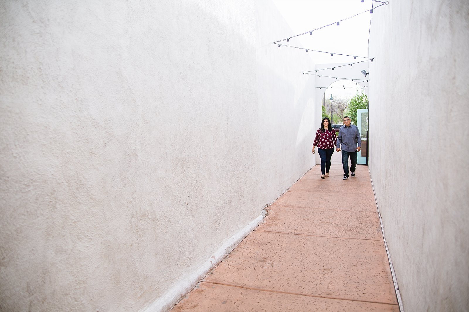 Couple walking down walkway during their Gilbert heritage district engagement session by wedding photographer PMA Photography.