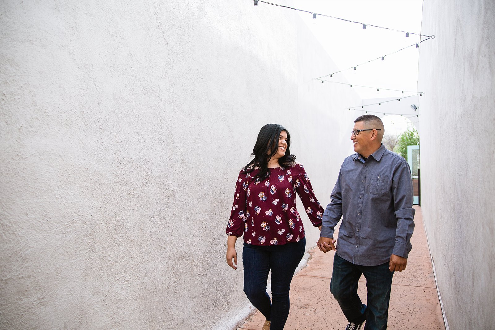 Couple walking down walkway during their Gilbert heritage district engagement session by wedding photographer PMA Photography.