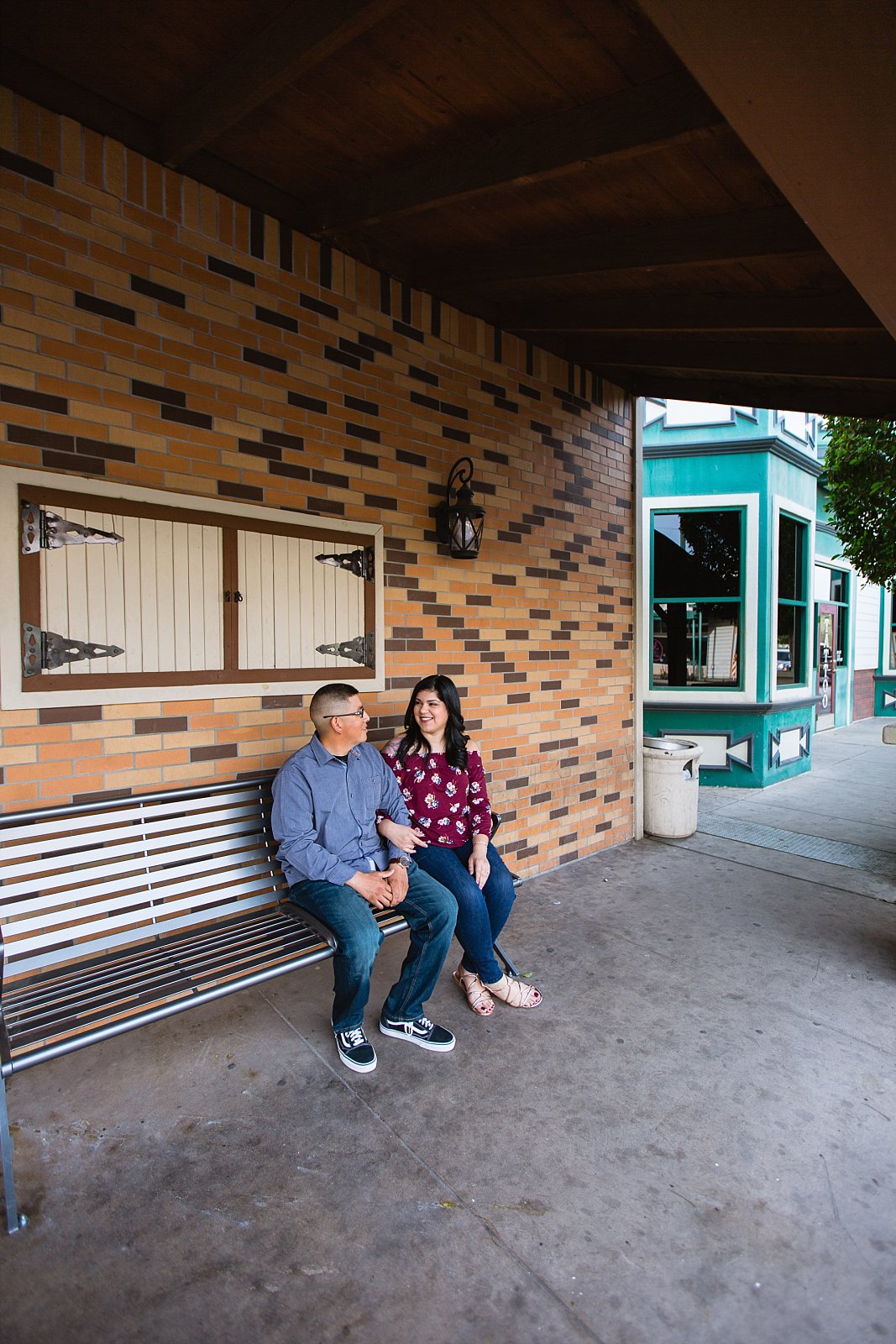Couple sitting on bench in Gilbert heritage district at their engagement session by wedding photographers PMA Photography.