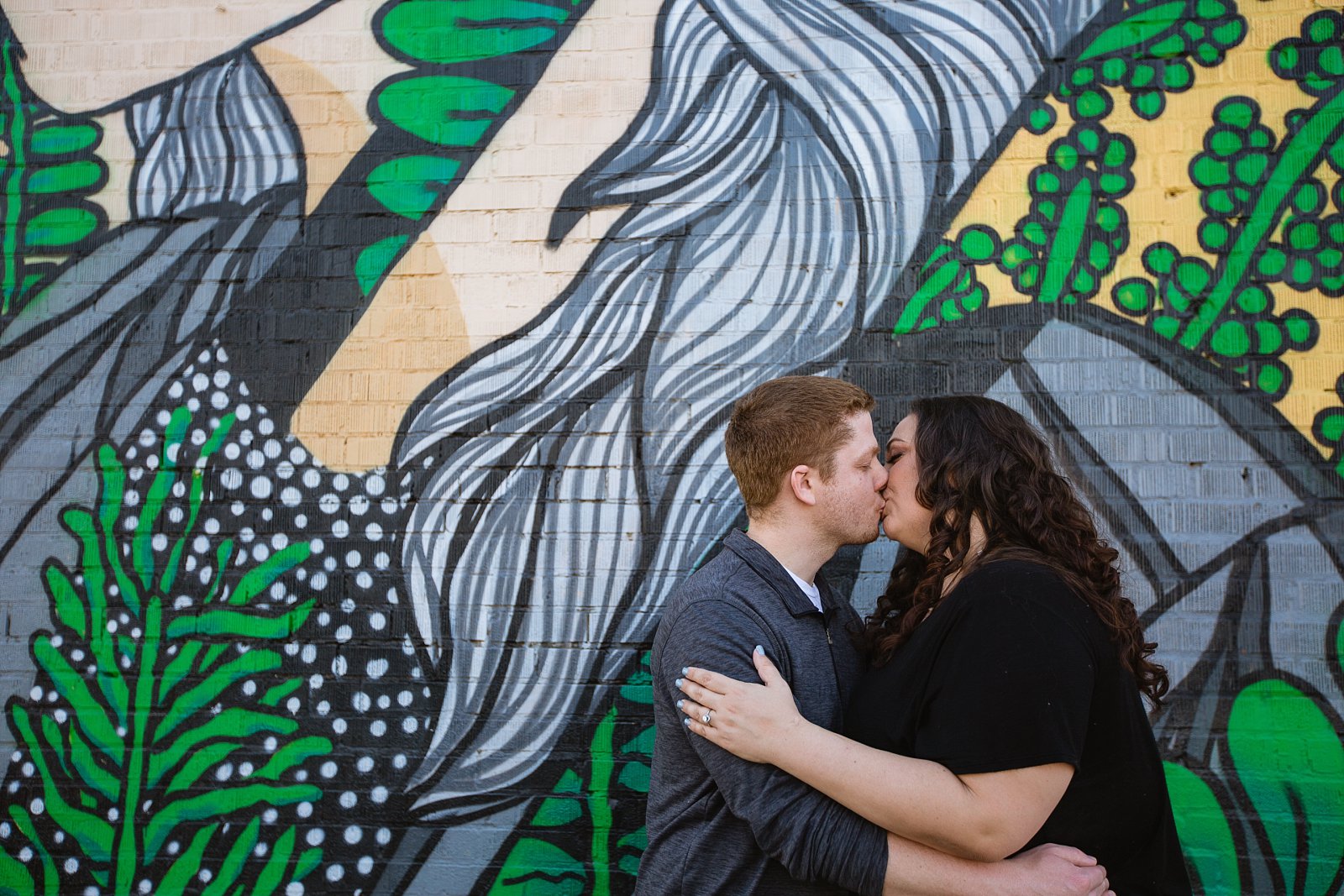 Couple kiss in front of art mural for their Roosevelt Row Art District engagement session by PMA Photography.