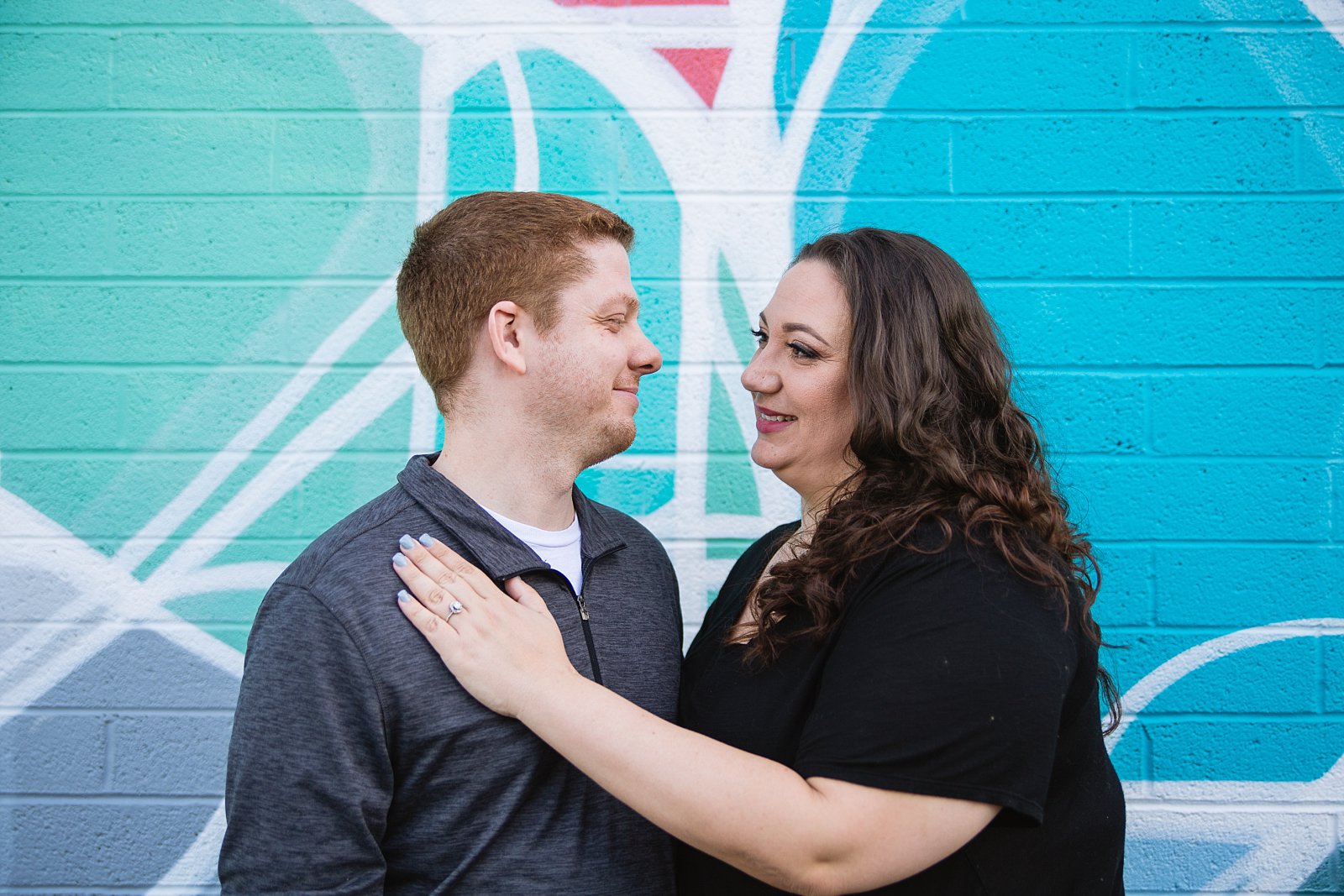 Couple looking at each other in front of art mural during their Roosevelt Row Art District engagement session by PMA Photography.