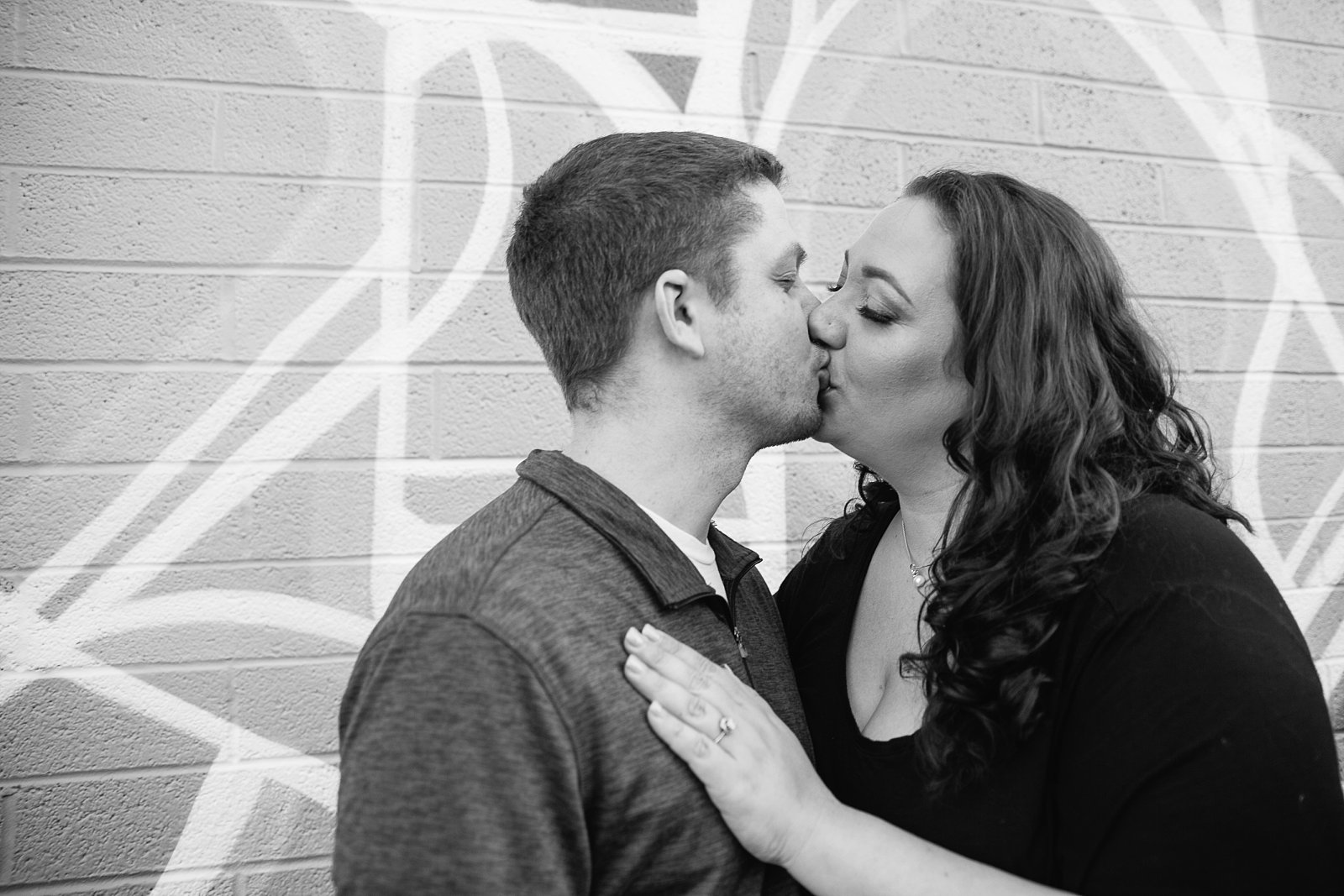 Black and white photograph of couple kissing in front of art mural during their Roosevelt Row Art District engagement session by PMA Photography.