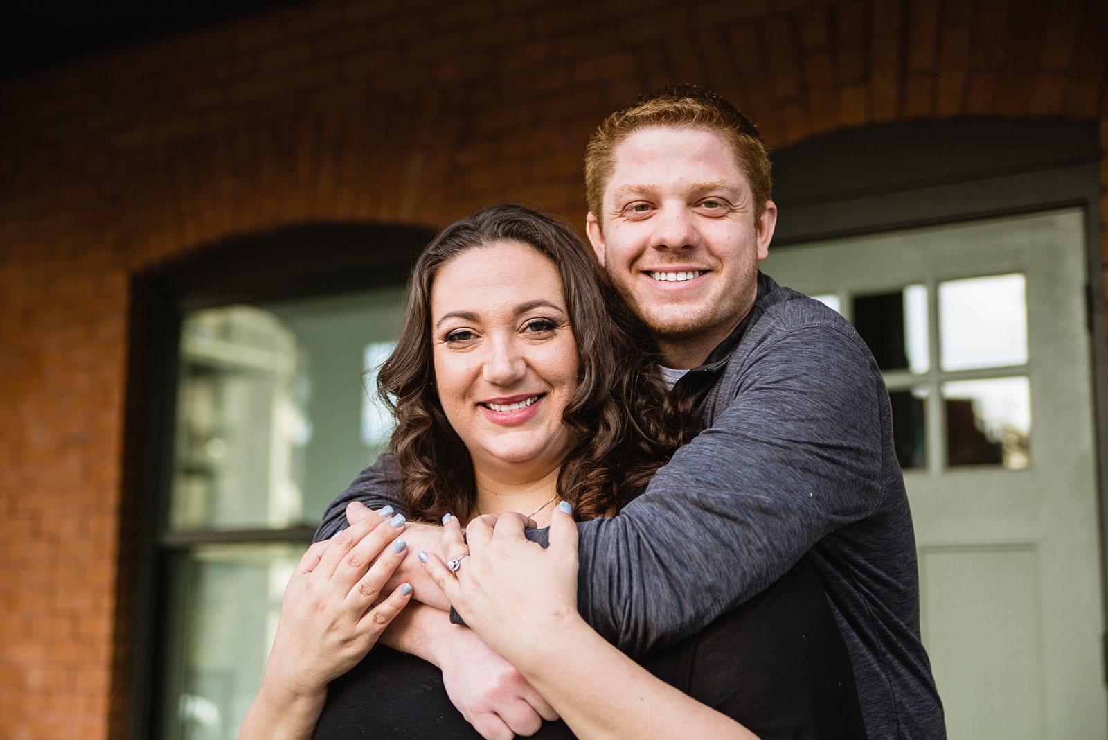 Couple posing in front of red brick building during their downtown Phoenix engagement session by PMA Photography.